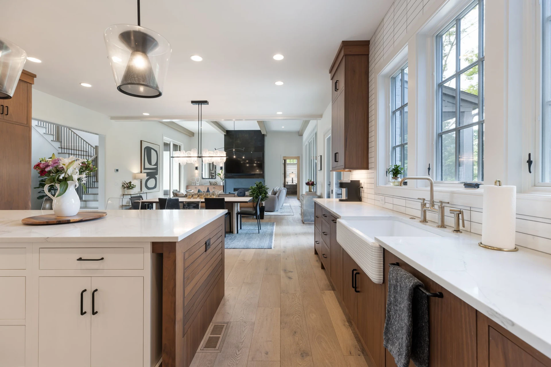 Kitchen with wood and white cabinets, two islands, farmhouse sink, and a view to a staircase and living room