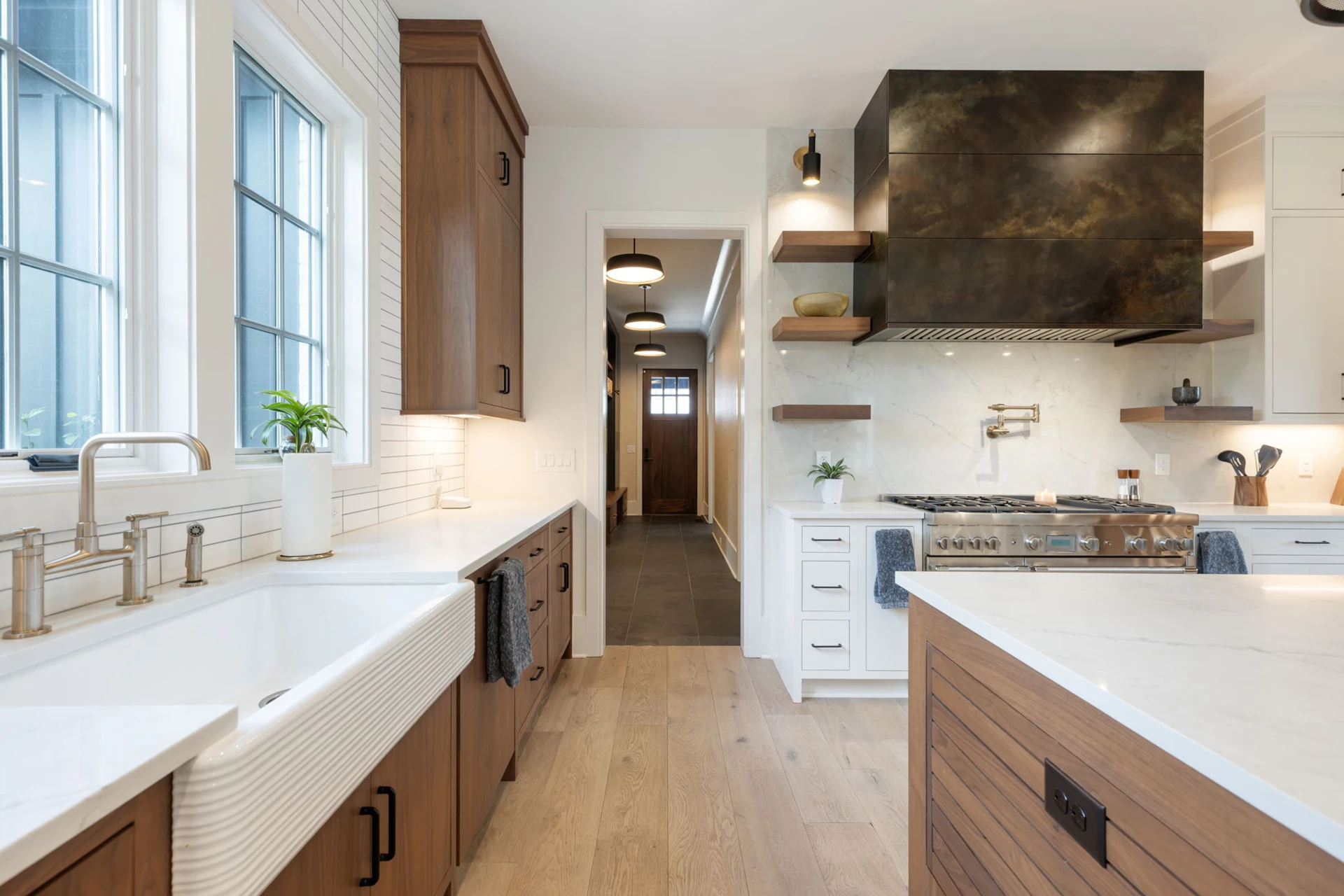 Galley kitchen with wood cabinets, white farmhouse sink under a black-grid window, and a dark metal range hood