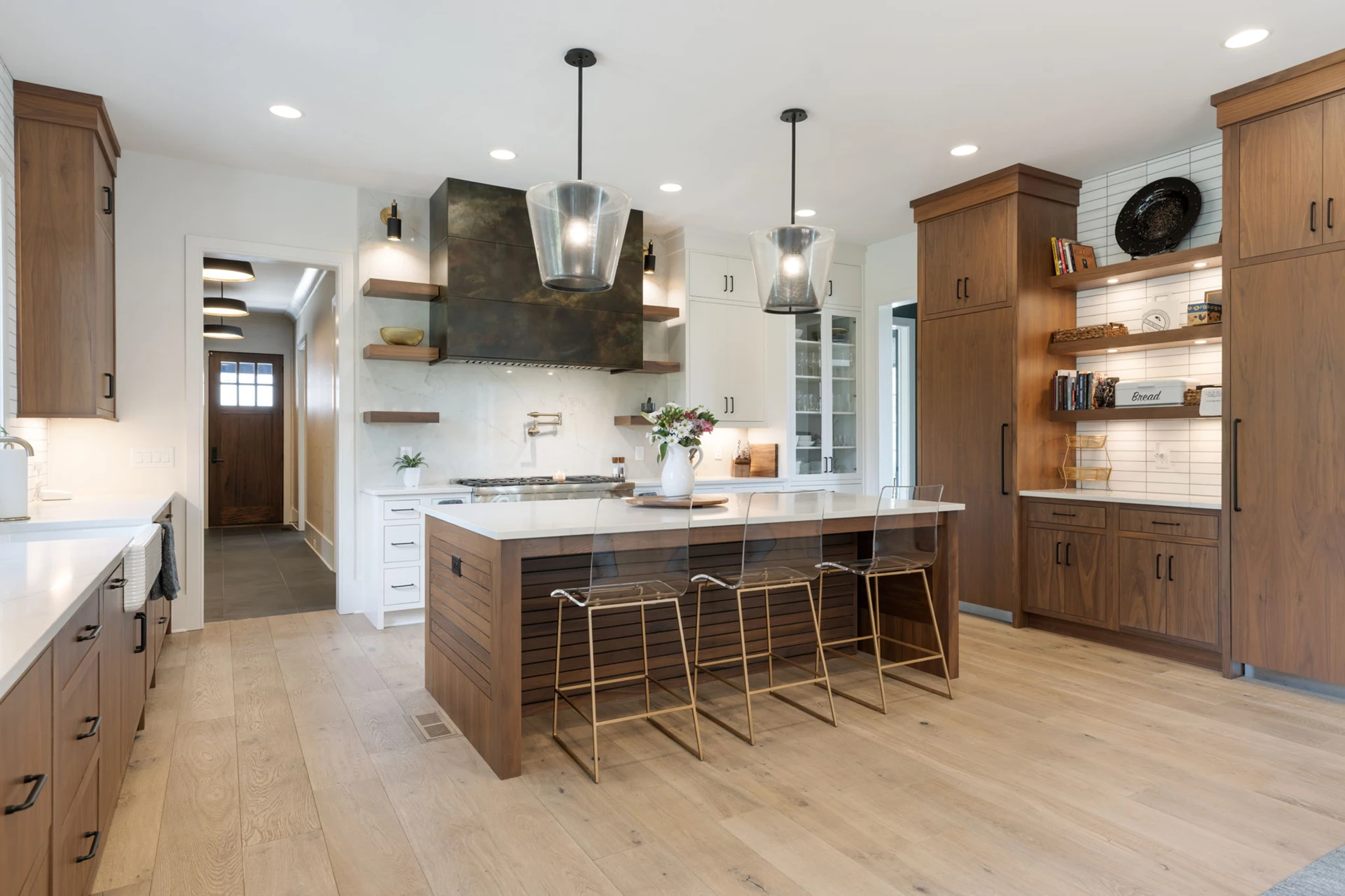 Kitchen with wood cabinets, black geometric pendants, dark metal range hood, and a wood island with brass-legged stools