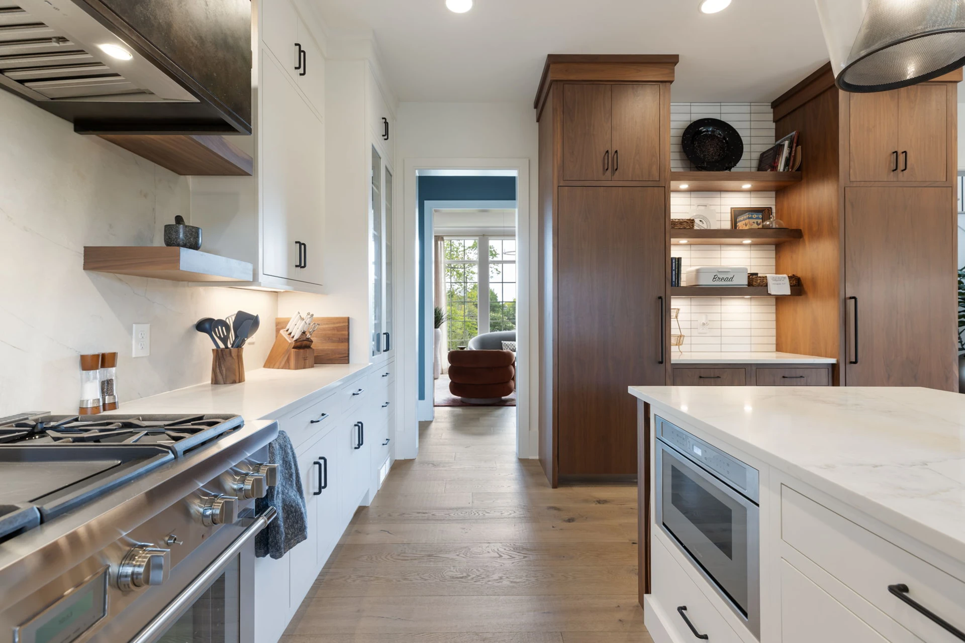 Kitchen corridor with stainless range and ovens, white and wood cabinets, and a built-in microwave in the island