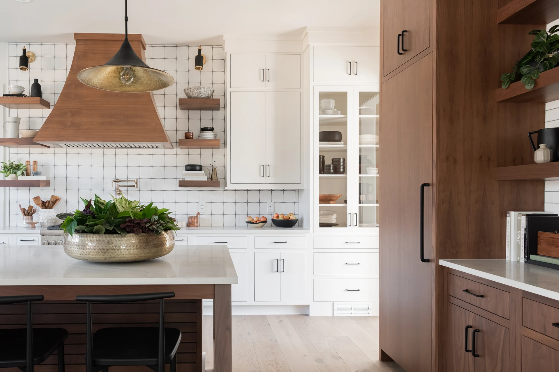 Kitchen with wood range hood, gold dome pendant, white grid-tile backsplash, and a wood island with brass bowl centerpiece