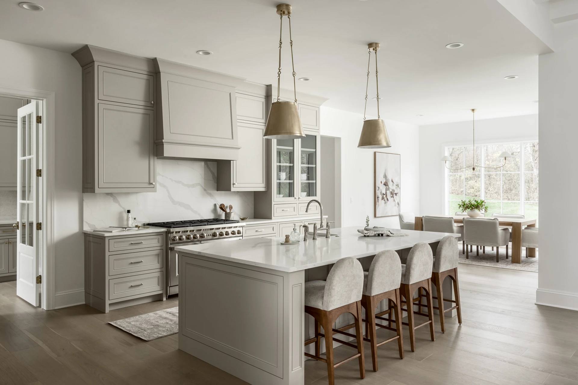 Gray kitchen with large island, gold pendants, upholstered stools, marble backsplash, and a dining area beyond