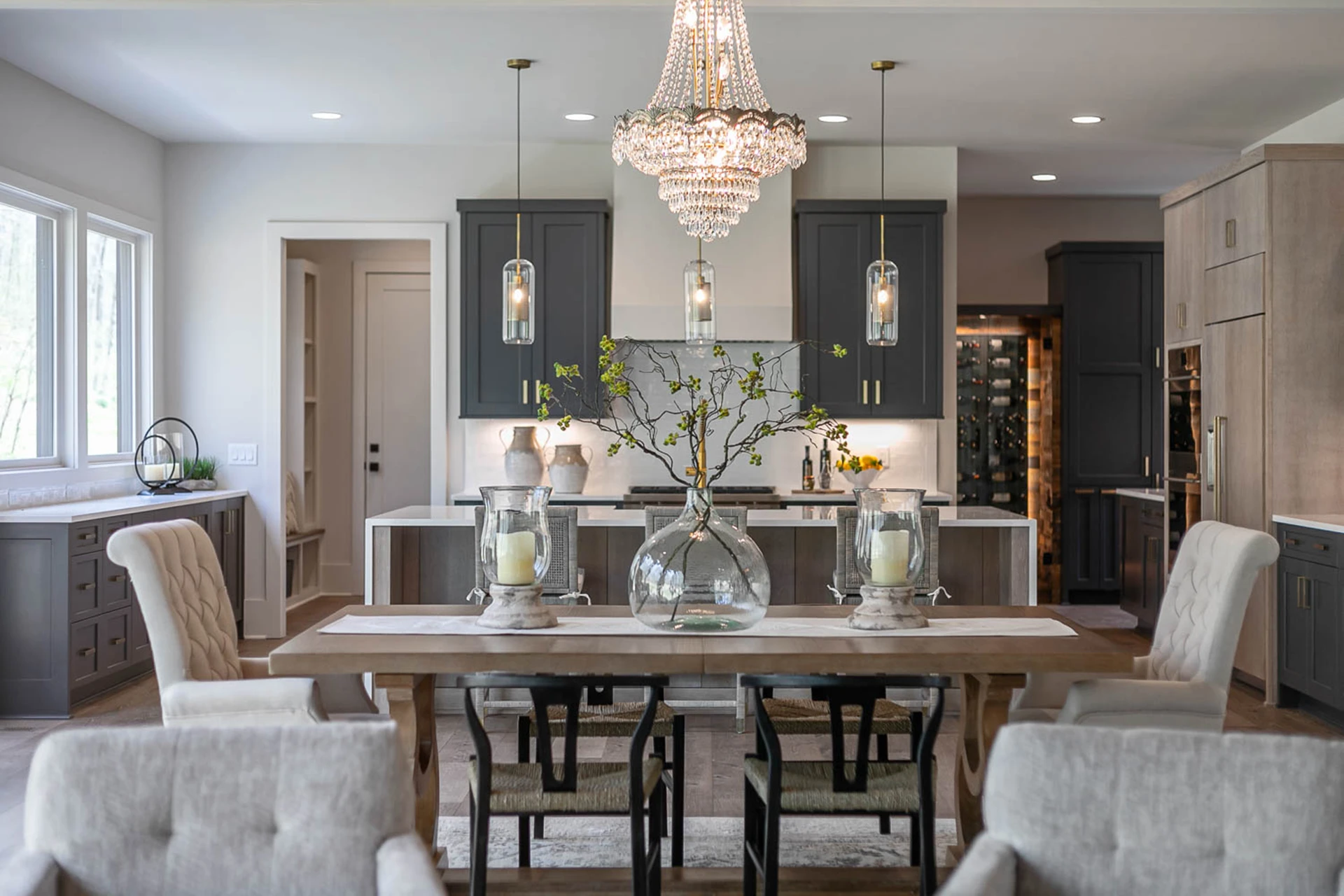 Dining and kitchen with crystal empire chandelier, glass pendants, gray cabinets, and a wood dining table