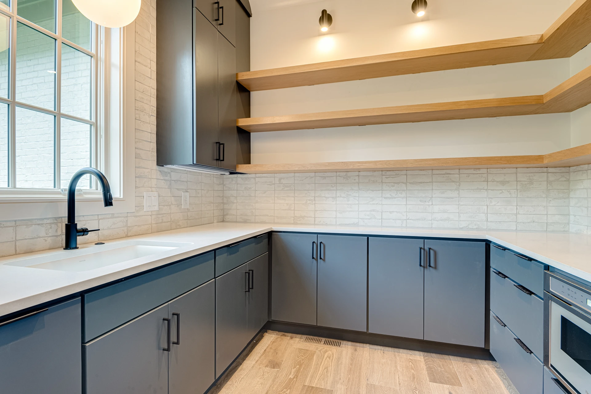 Scullery with navy cabinets, floating wood shelves, white tile, black faucet, and a globe pendant