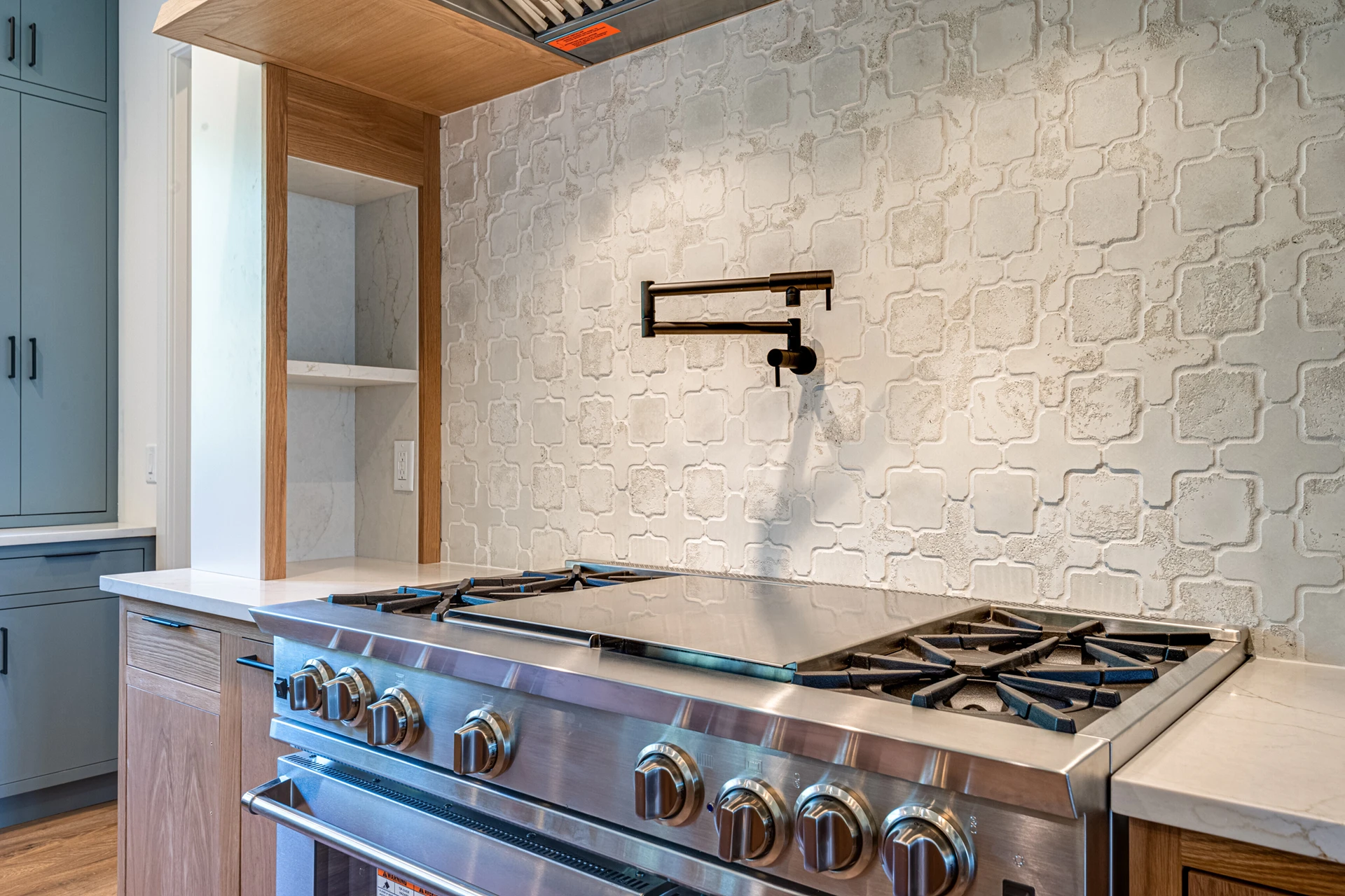 Close-up of a stainless gas cooktop with black pot-filler faucet and white arabesque tile backsplash