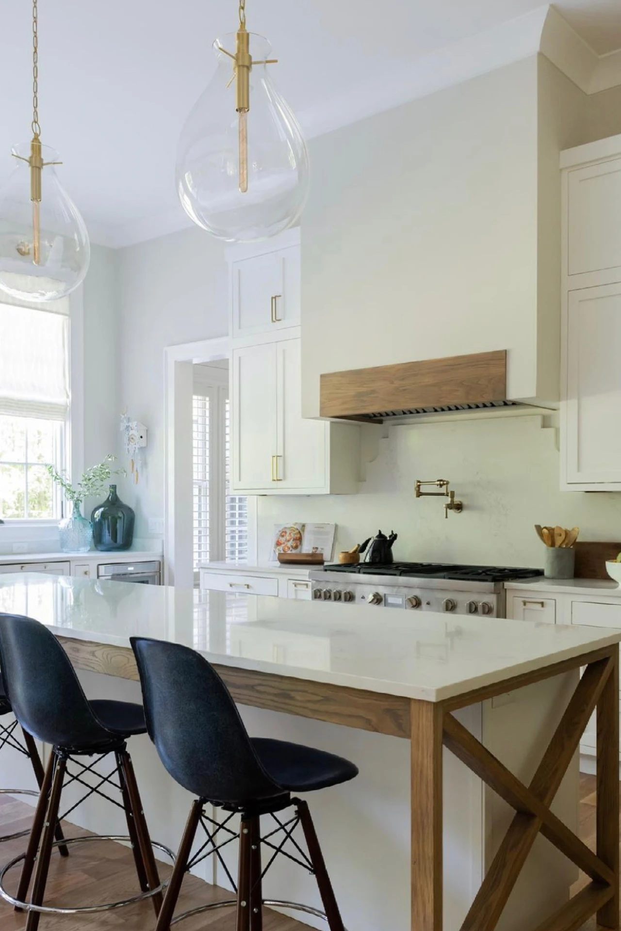 Kitchen with glass pendants, wood range hood, white cabinets, and a wood X-leg island with black chairs