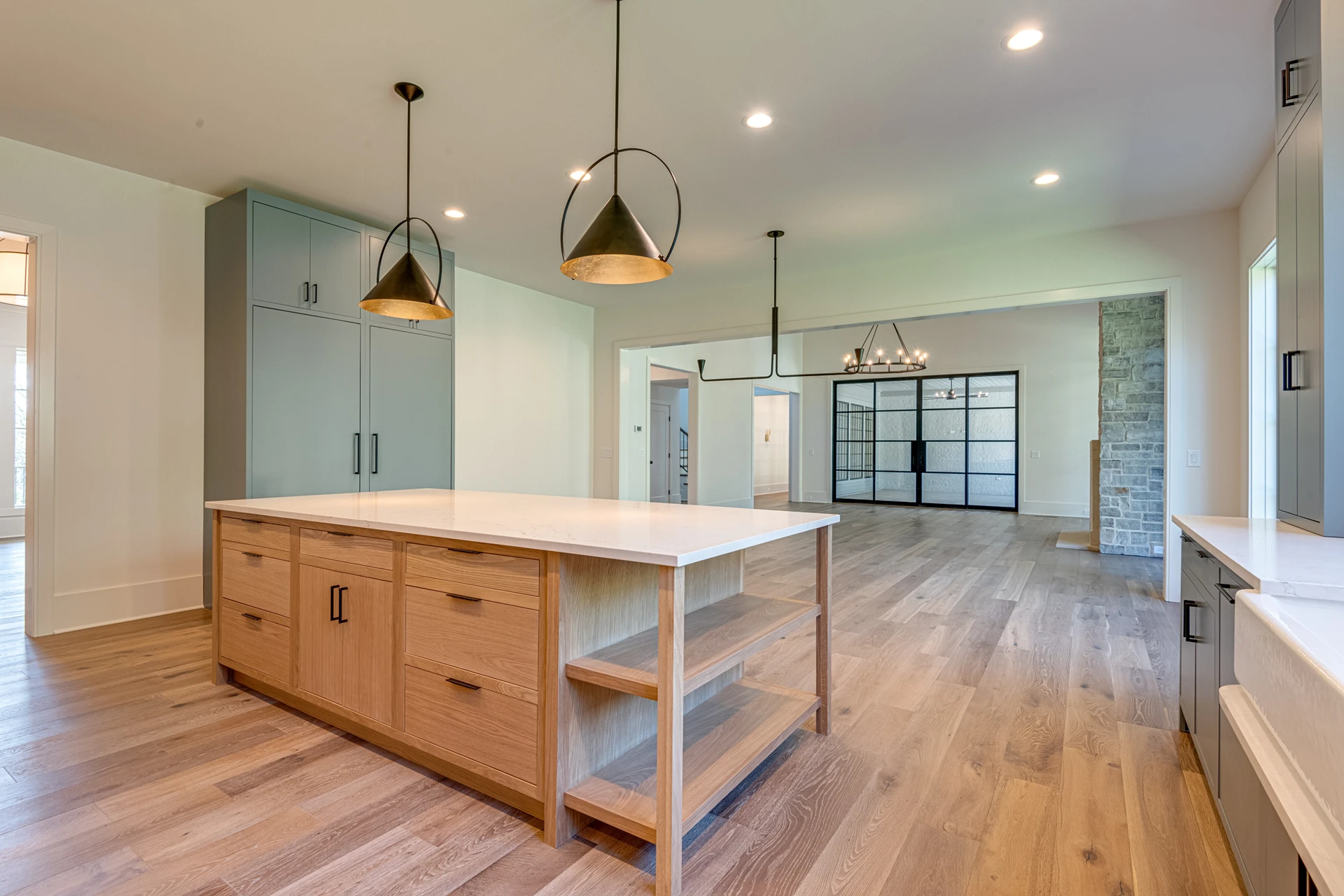 Kitchen with light wood island and open shelving, black cone pendants, sage cabinets, and black-framed glass doors