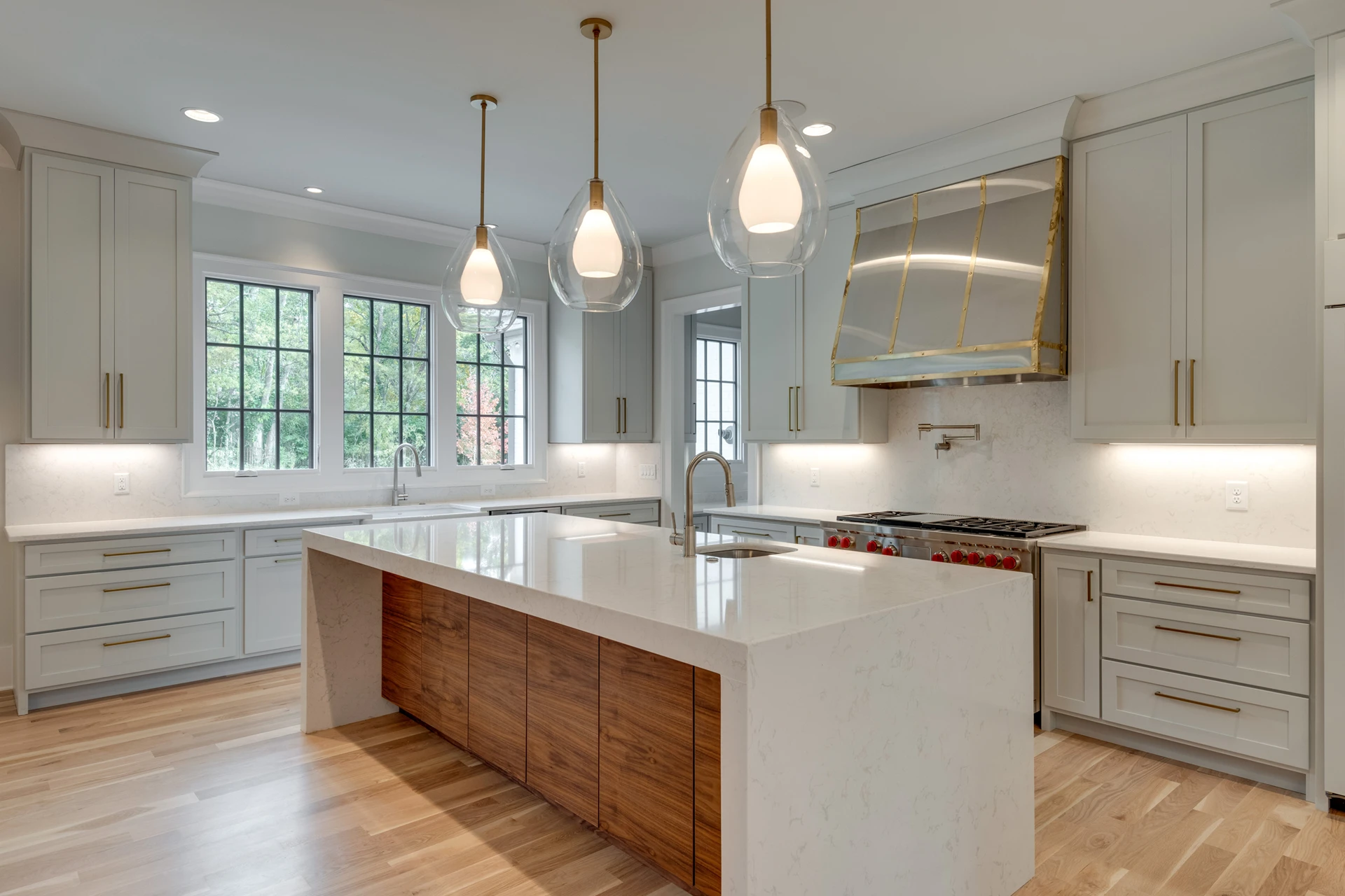 Kitchen with gray cabinets, gold-accented range hood, glass globe pendants, and a wood waterfall island