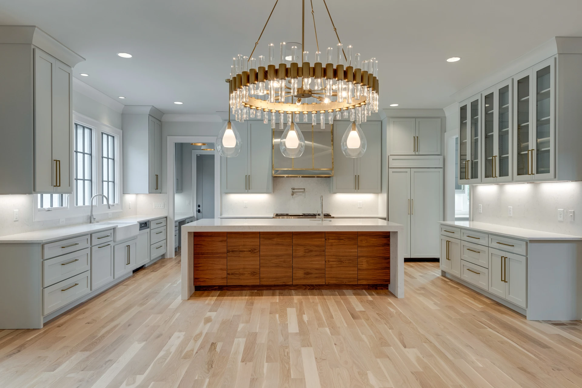 Gray kitchen with gold drum chandelier, glass pendants, wood island, farmhouse sink, and glass-front refrigerator