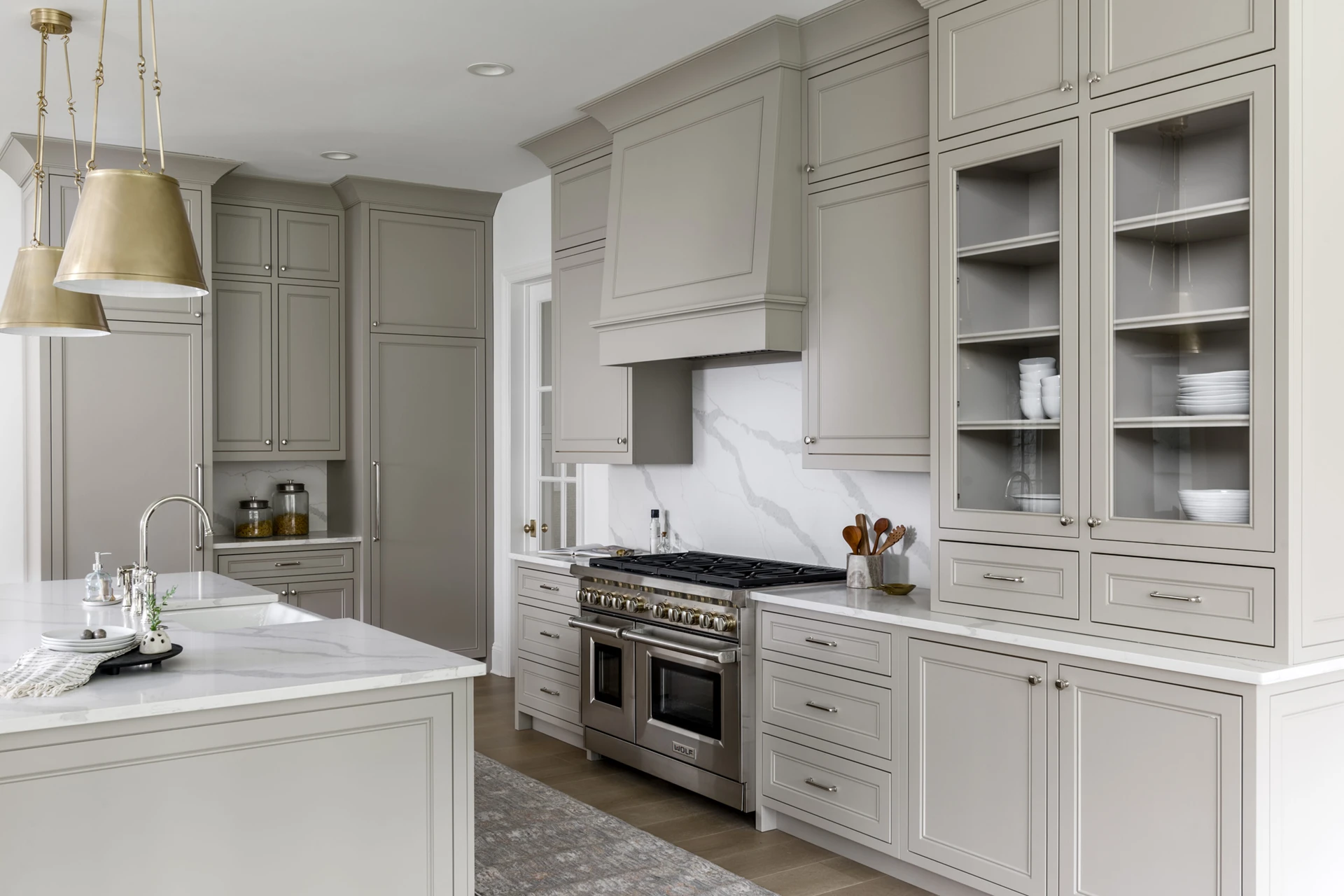 Greige kitchen with paneled range hood, marble backsplash, professional stainless range, and glass-front cabinets