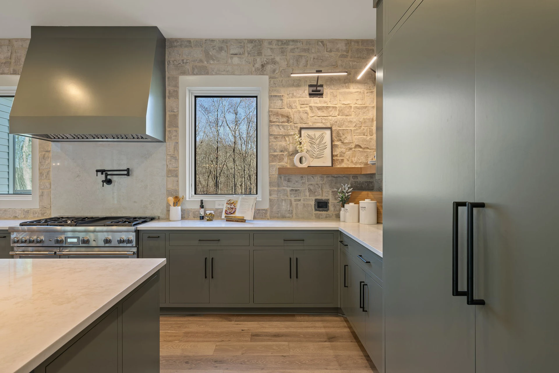 Kitchen with gray cabinets, gray range hood, stone backsplash, stainless range, and a pot filler