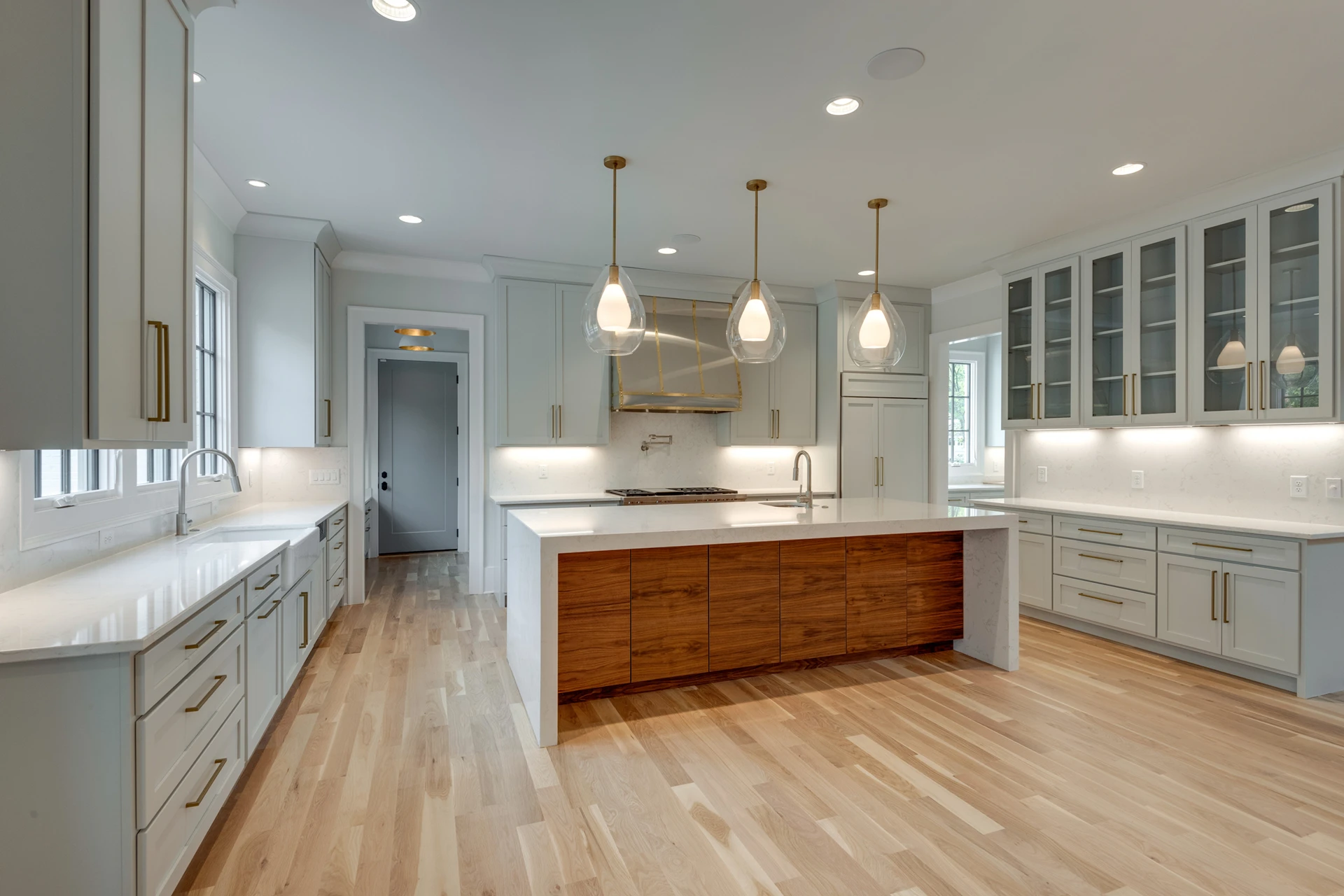 Light gray kitchen with three glass globe pendants, wood island, glass-front cabinets, and a stainless range