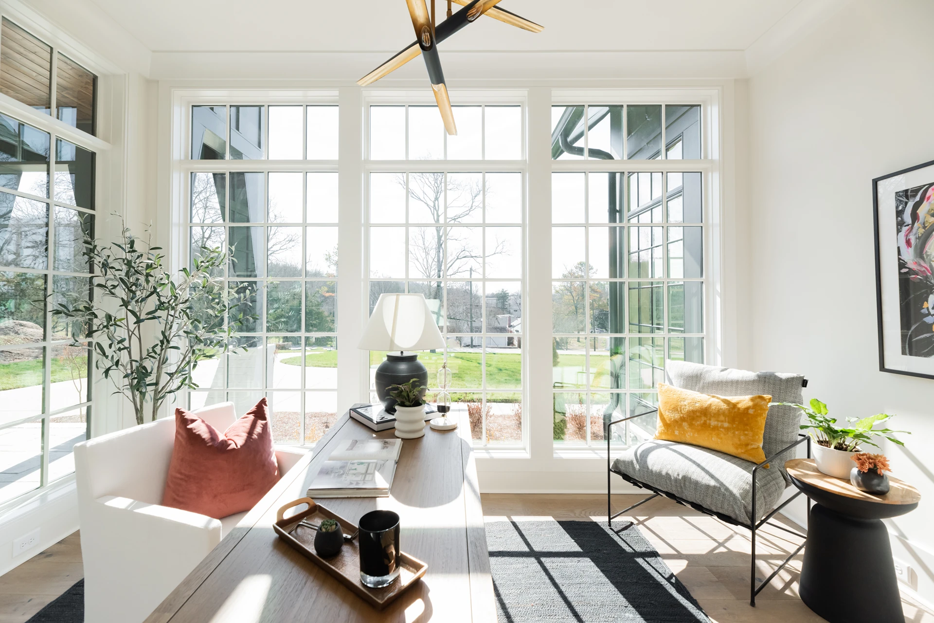Sunroom nook with wall of windows, built-in bench with pillows, twig chandelier, and a round coffee table