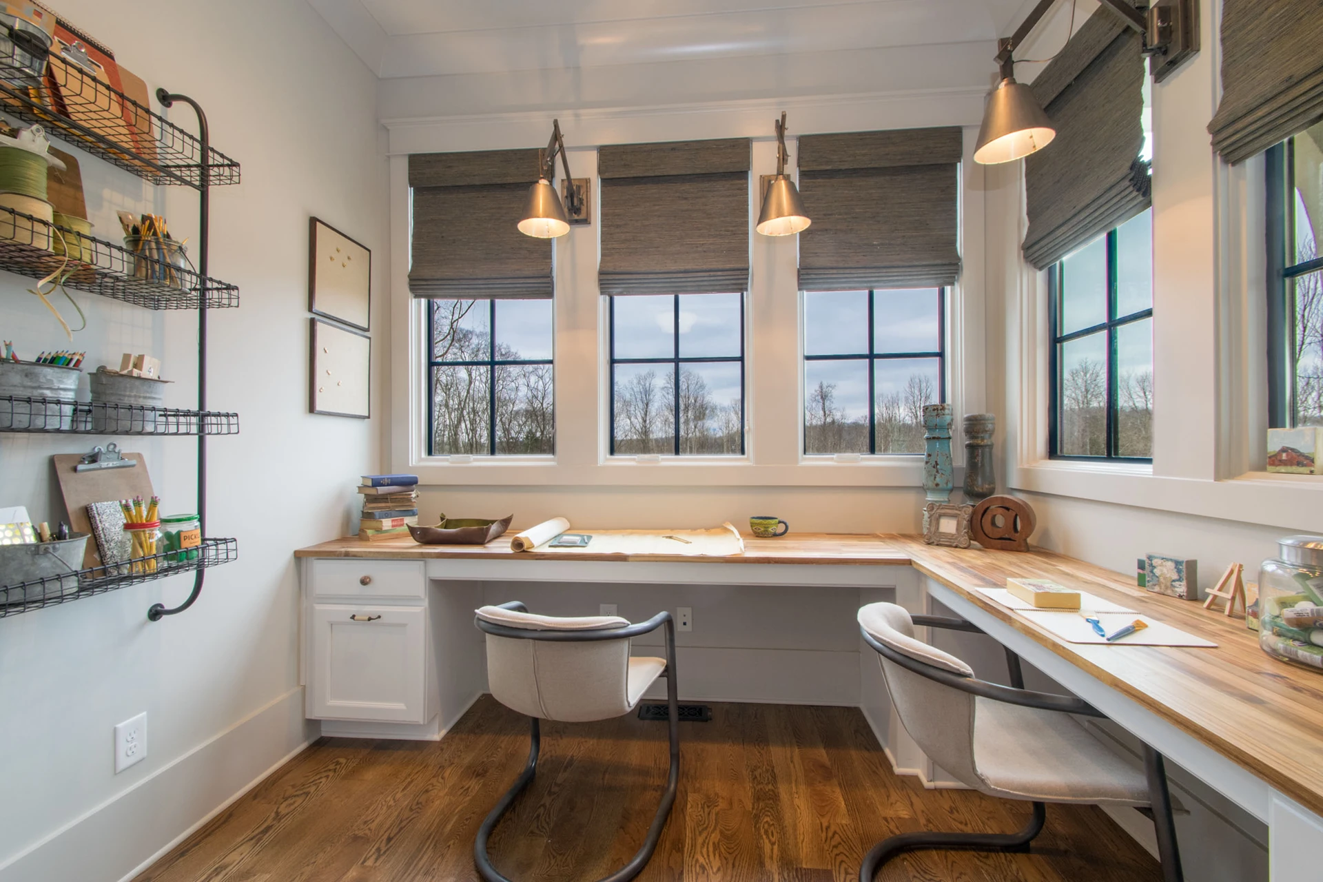 Craft room with butcher-block L-shaped desk, Roman shades, wire wall organizers, and pendant task lights