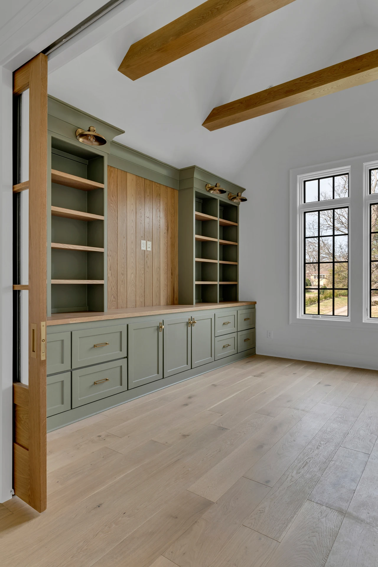 Empty room with green-and-wood built-in cabinetry, ceiling beams, and a black-grid window