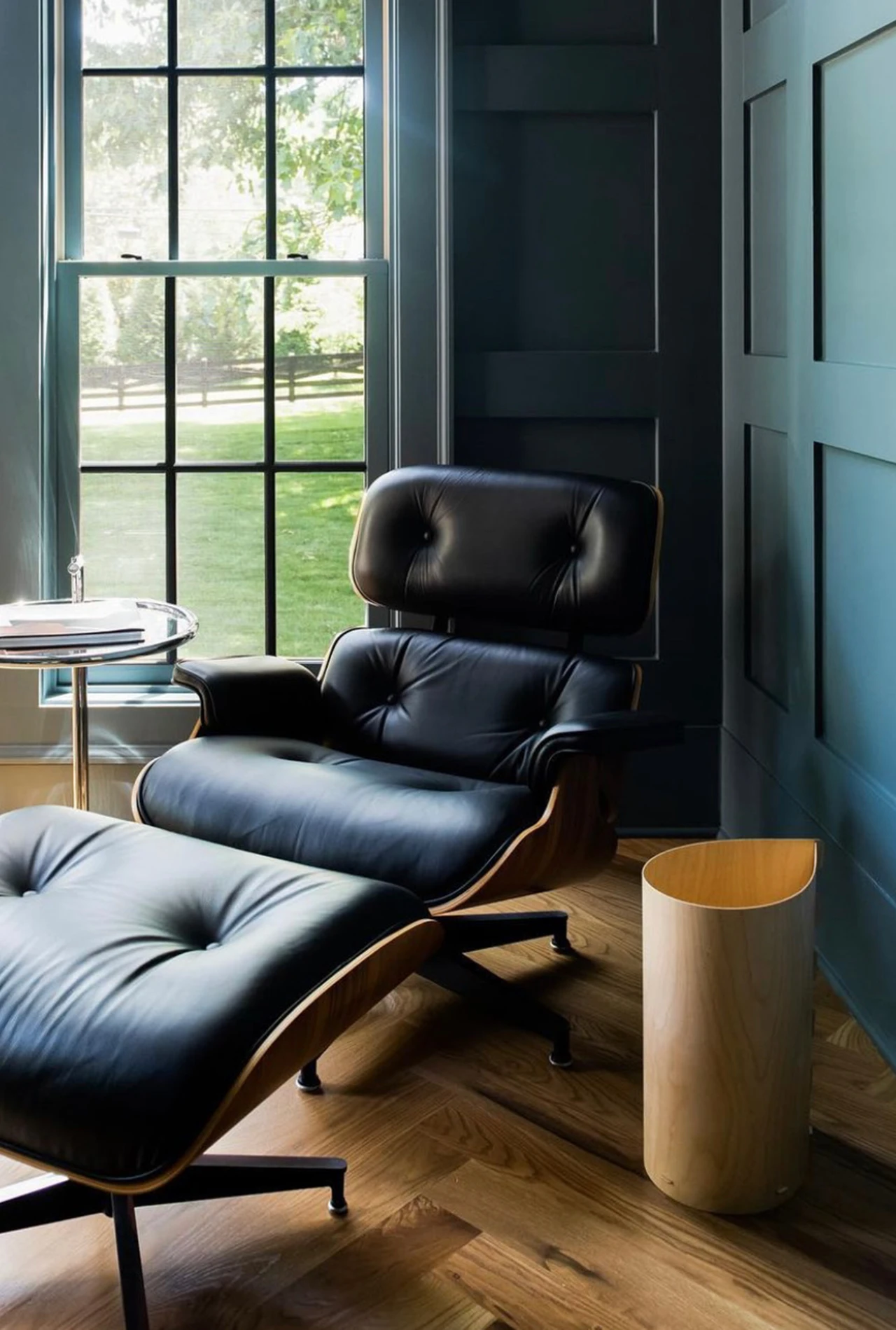 Black leather lounge chair and ottoman by a window with teal paneled walls