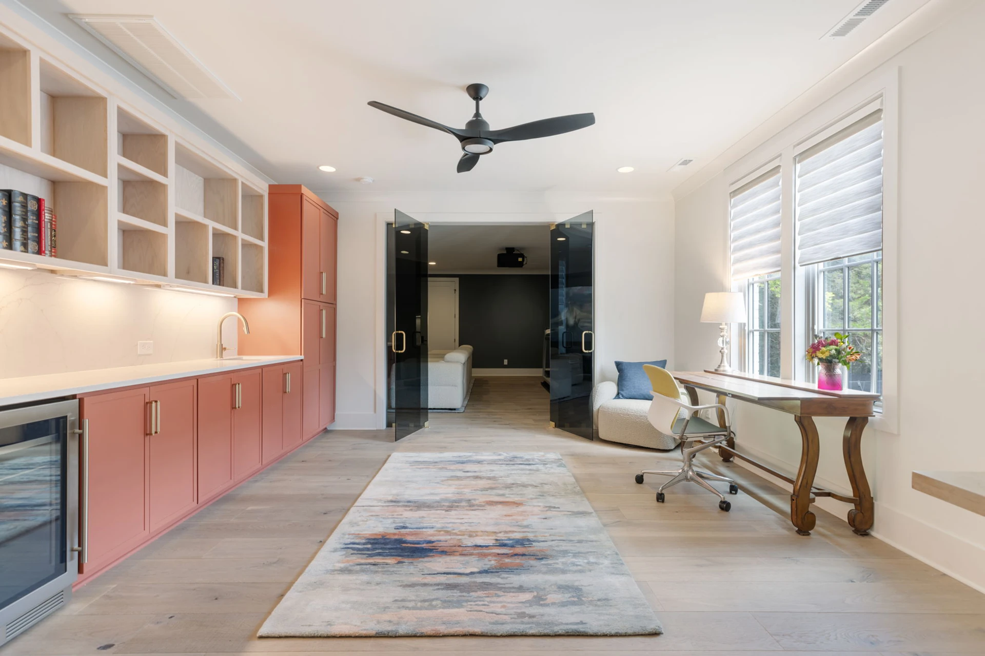 Bonus room with terracotta cabinets, open shelving, beverage fridge, ceiling fan, and a glass door to a media room