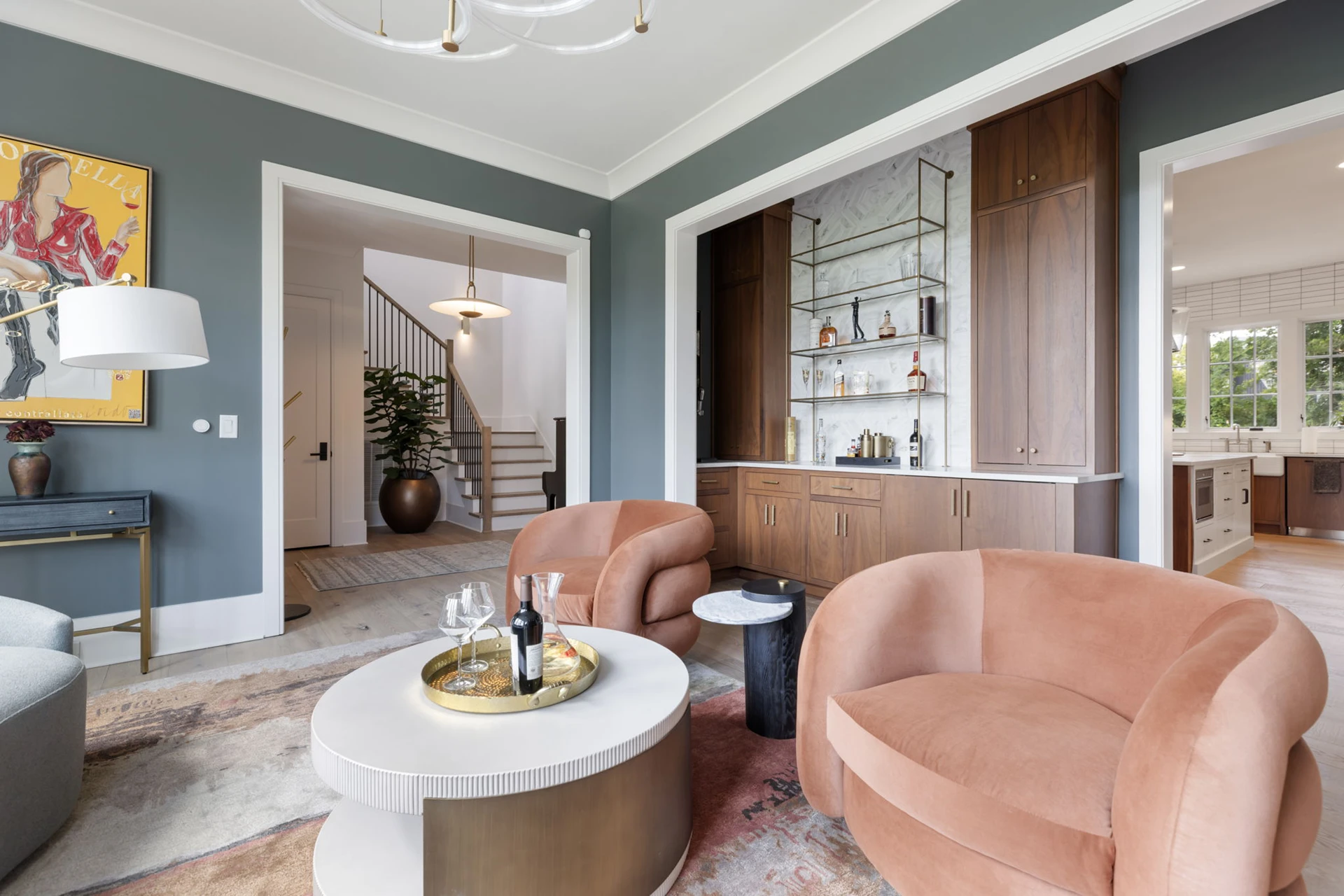Sitting room with gray-green walls, rust velvet chairs, and a wet bar, with views to a staircase and kitchen