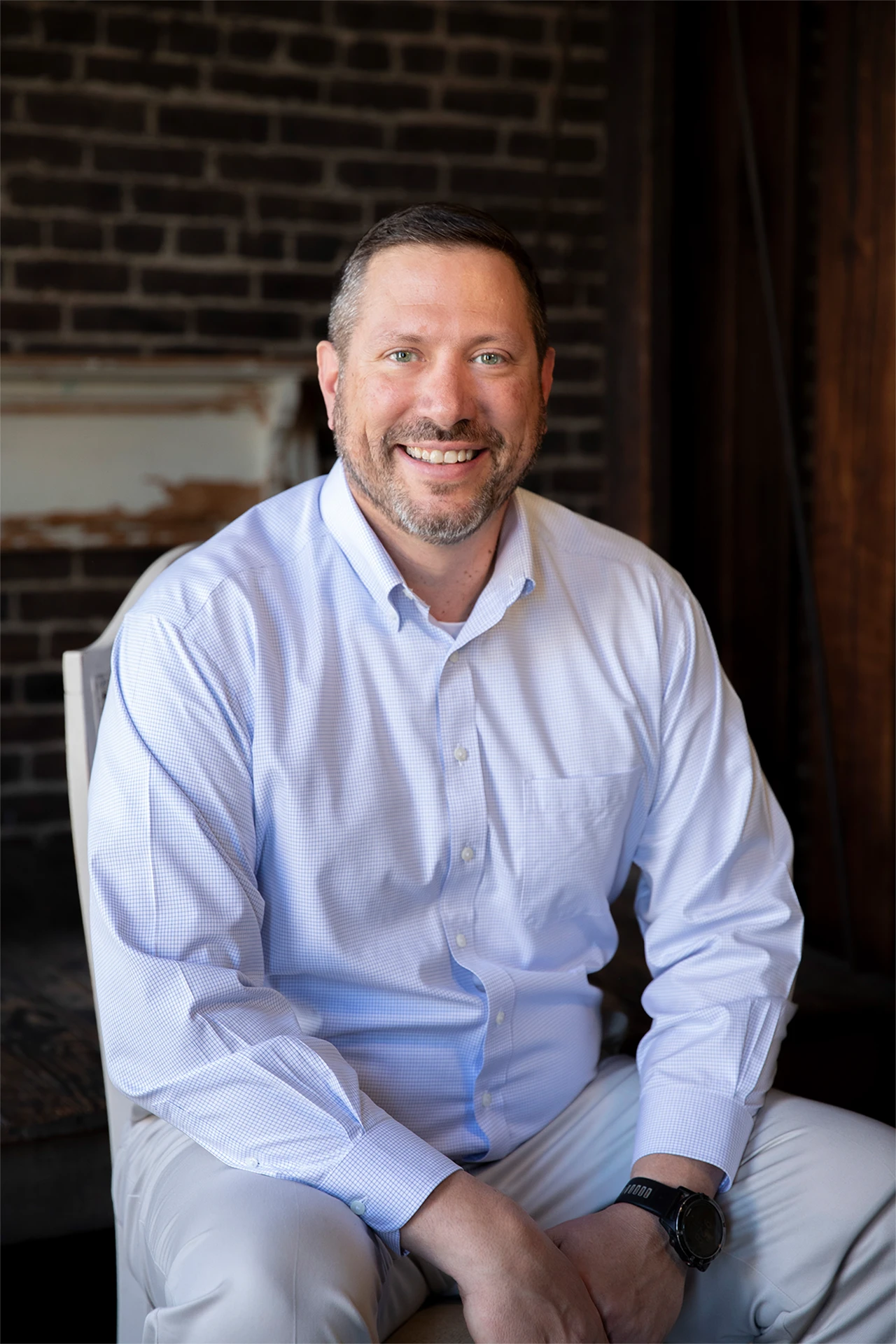 Professional headshot of a smiling man in a white shirt against an exposed brick wall