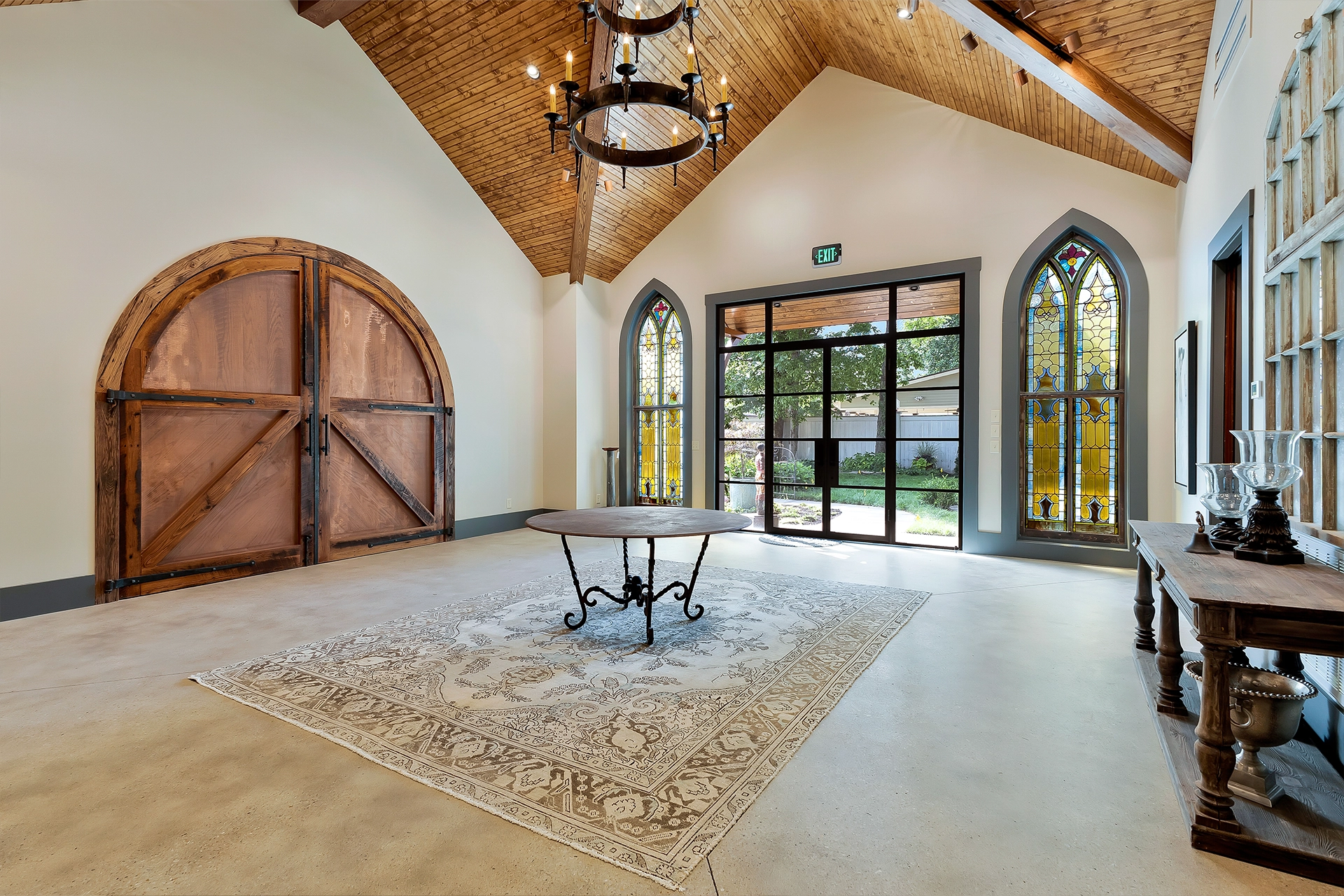 Great room with vaulted wood ceiling, arched barn doors, Gothic arched windows, and an iron chandelier