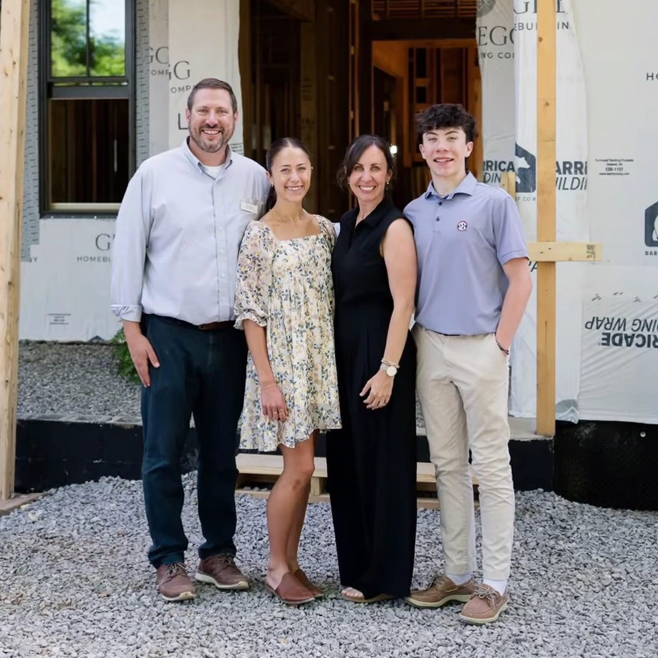 Family of four smiling in front of a home under construction with house wrap visible
