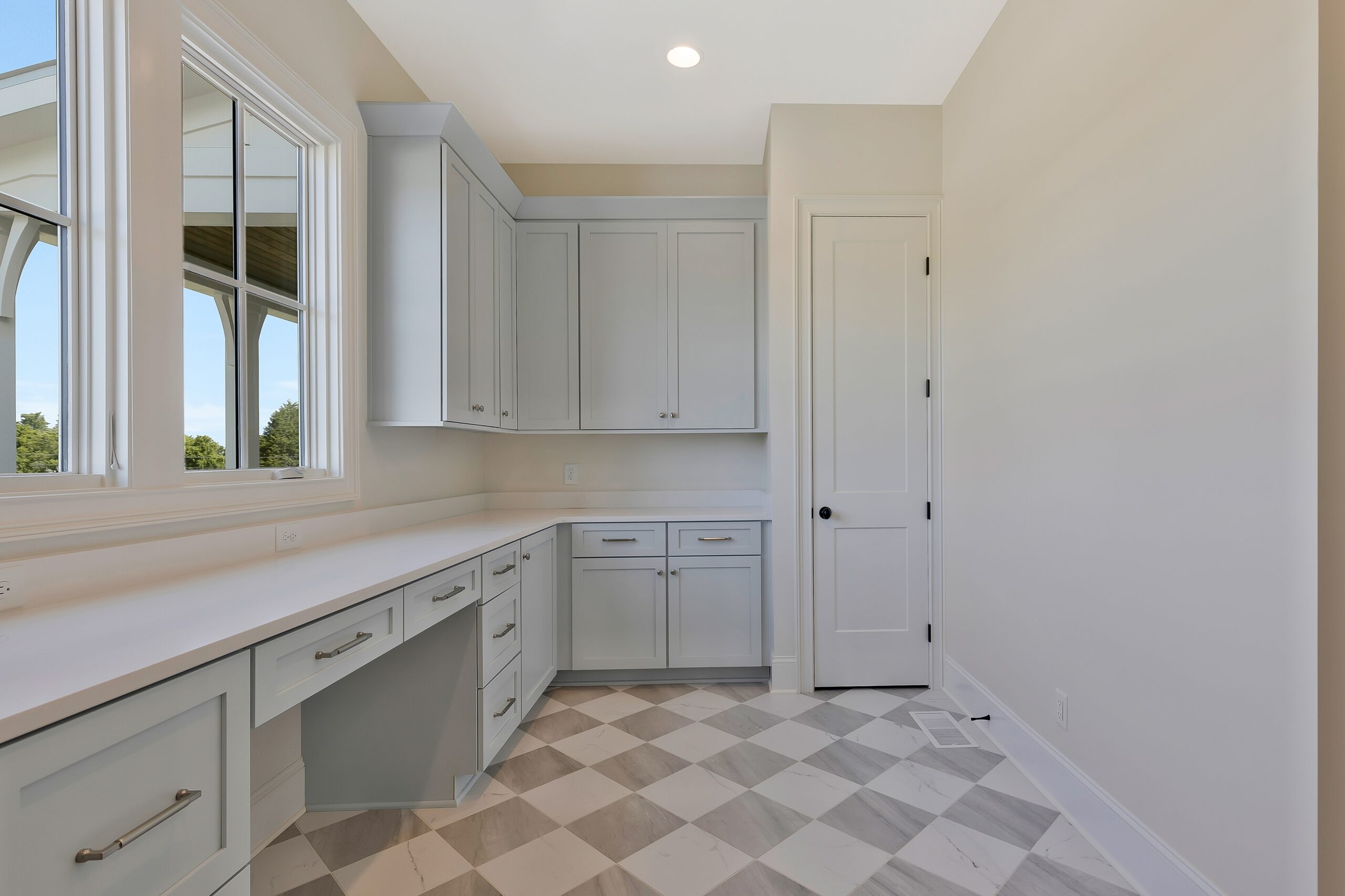 Creamy, white painted laundry room with pale blue cabinetry, a window, and tan and white checkered flooring