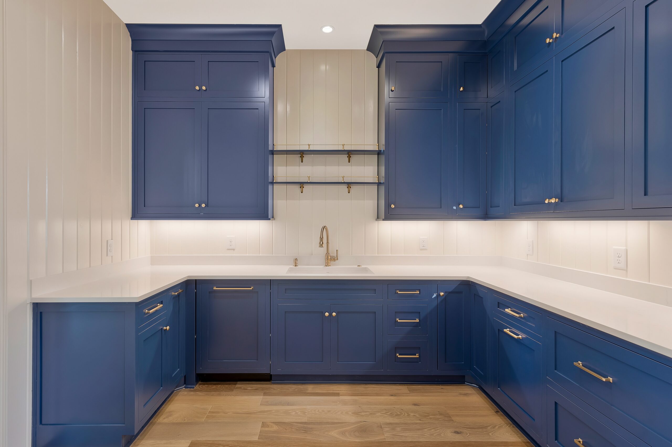 Navy cabinetry with light countertops and backspash, with light wood stained open shelving and sconce lighting