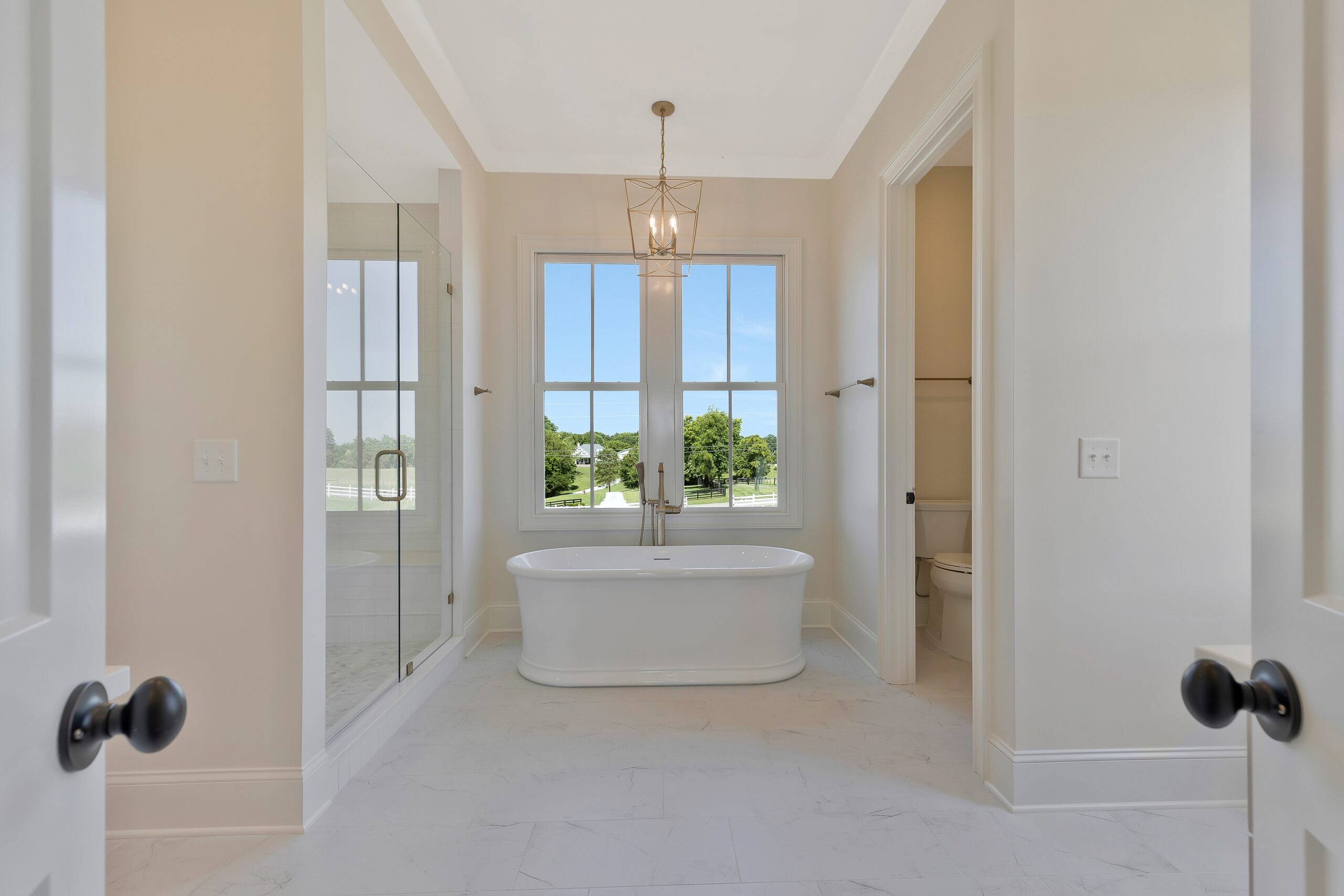 Master bath with freestanding tub under large paneled window and a marble glass walk-in shower