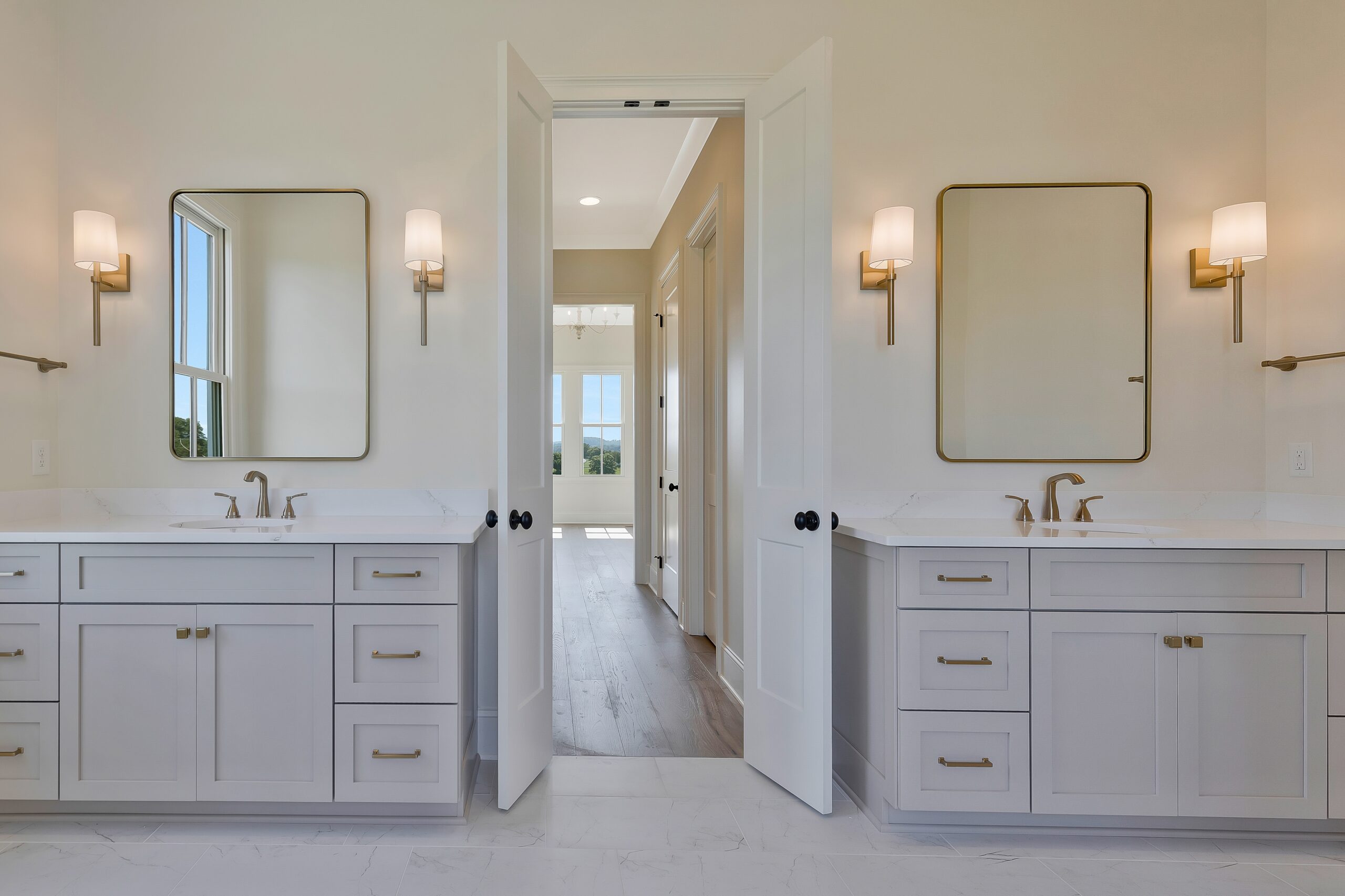 Dual-vanity bathroom with two gray vanities, marble tops, and a doorway to bedroom