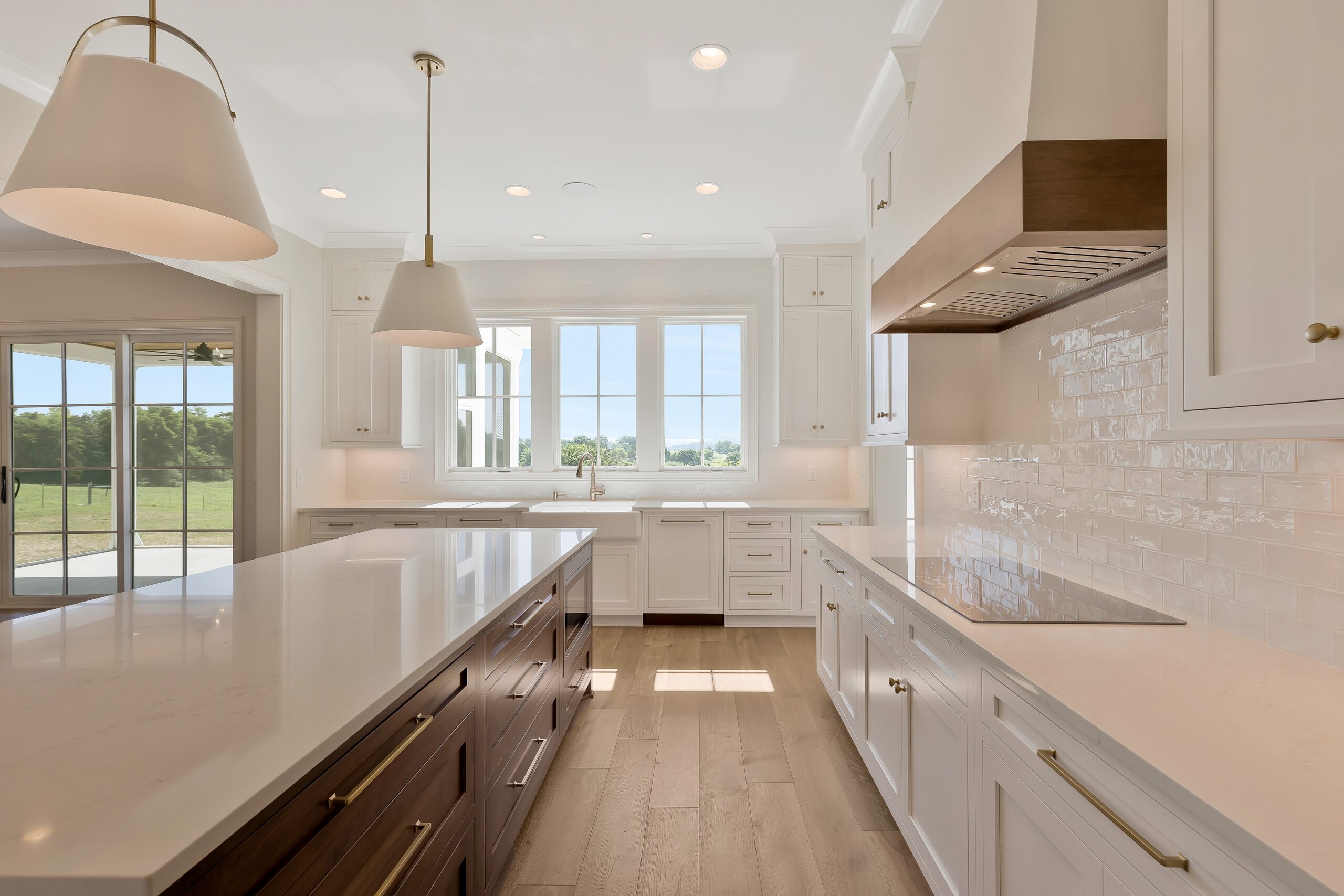 White kitchen with wood stained island with white pendant lights and row of windows