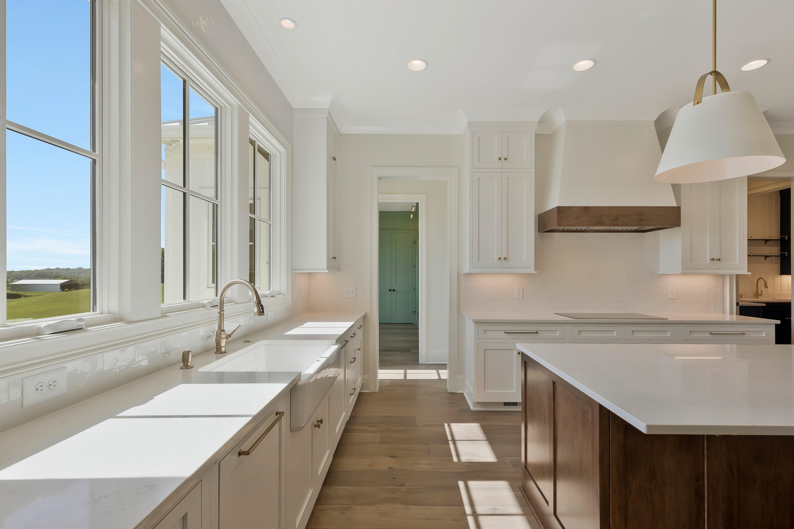 Corridor of white kitchen with wood stained island with white pendant lights and row of windows