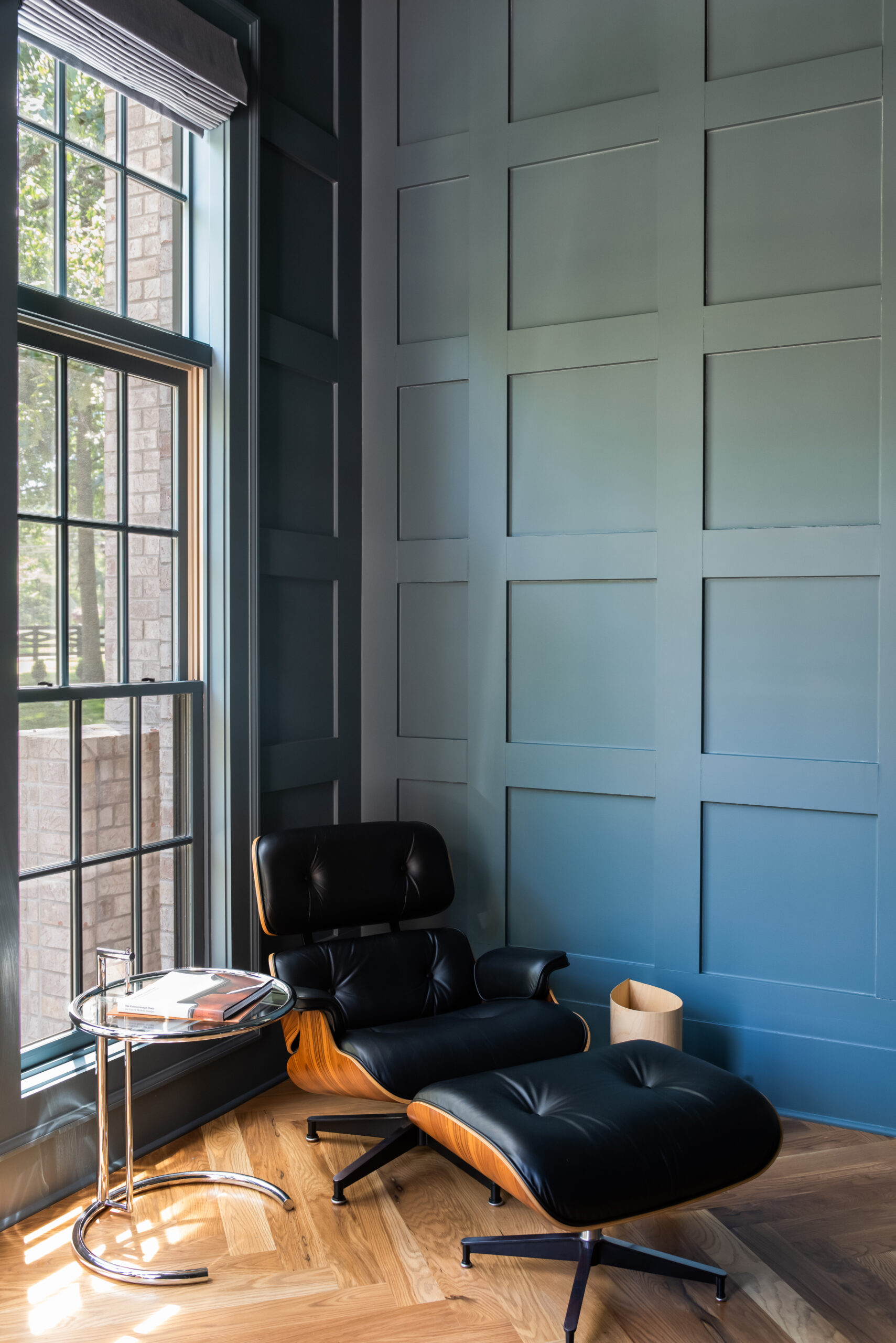 Black leather lounge chair and ottoman by a window with teal paneled walls
