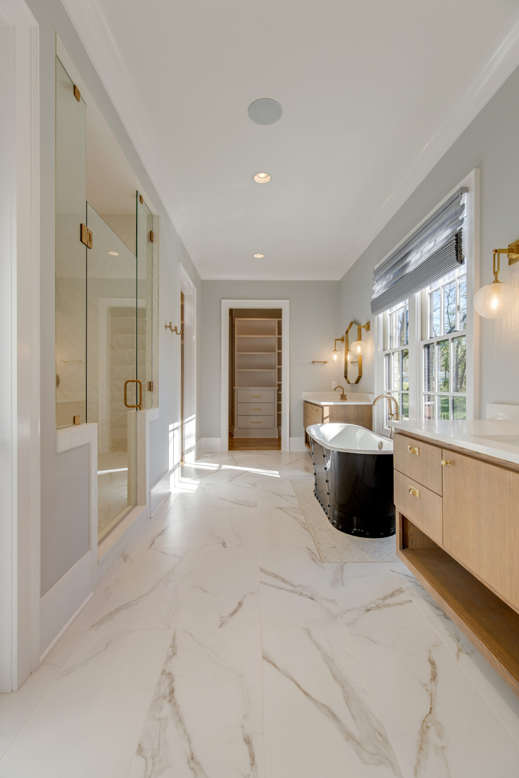 Corridor view of bathroom with dual light wood floating vanity and dark metal tub with glass front shower and view of closet
