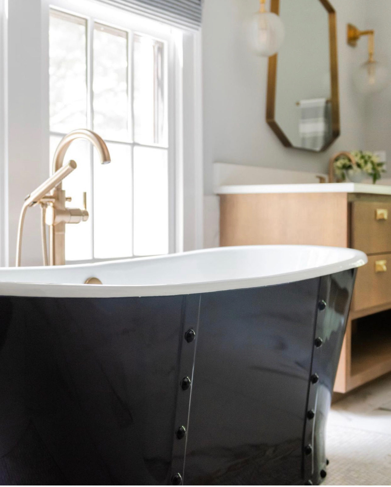Corridor view of bathroom with dual light wood floating vanity and dark metal tub