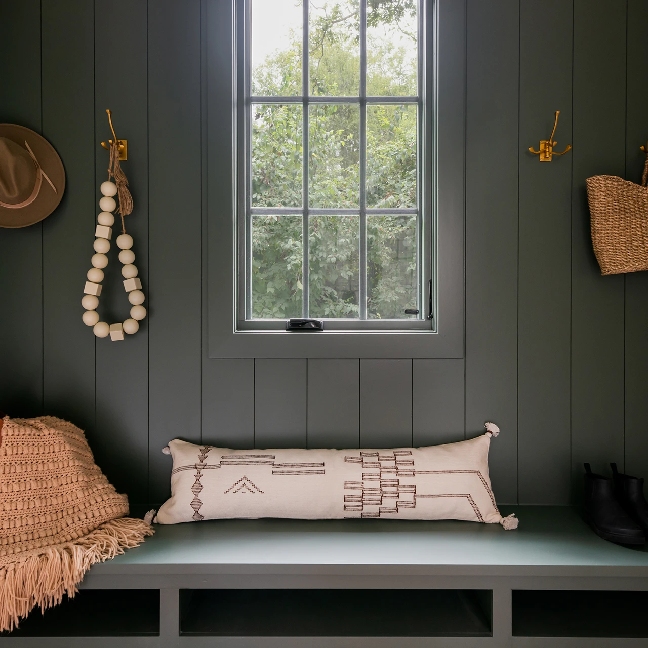 Mudroom nook with dark green walls, built-in bench, brass hooks, and a window