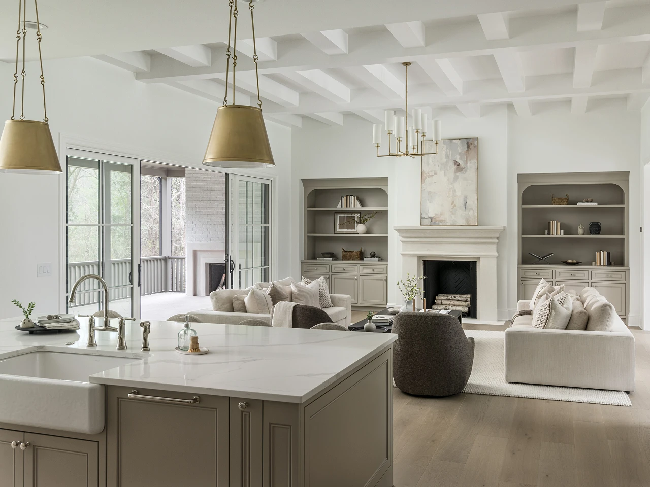Open-concept great room with vaulted beamed ceiling, stone fireplace, built-in shelving, and marble kitchen island