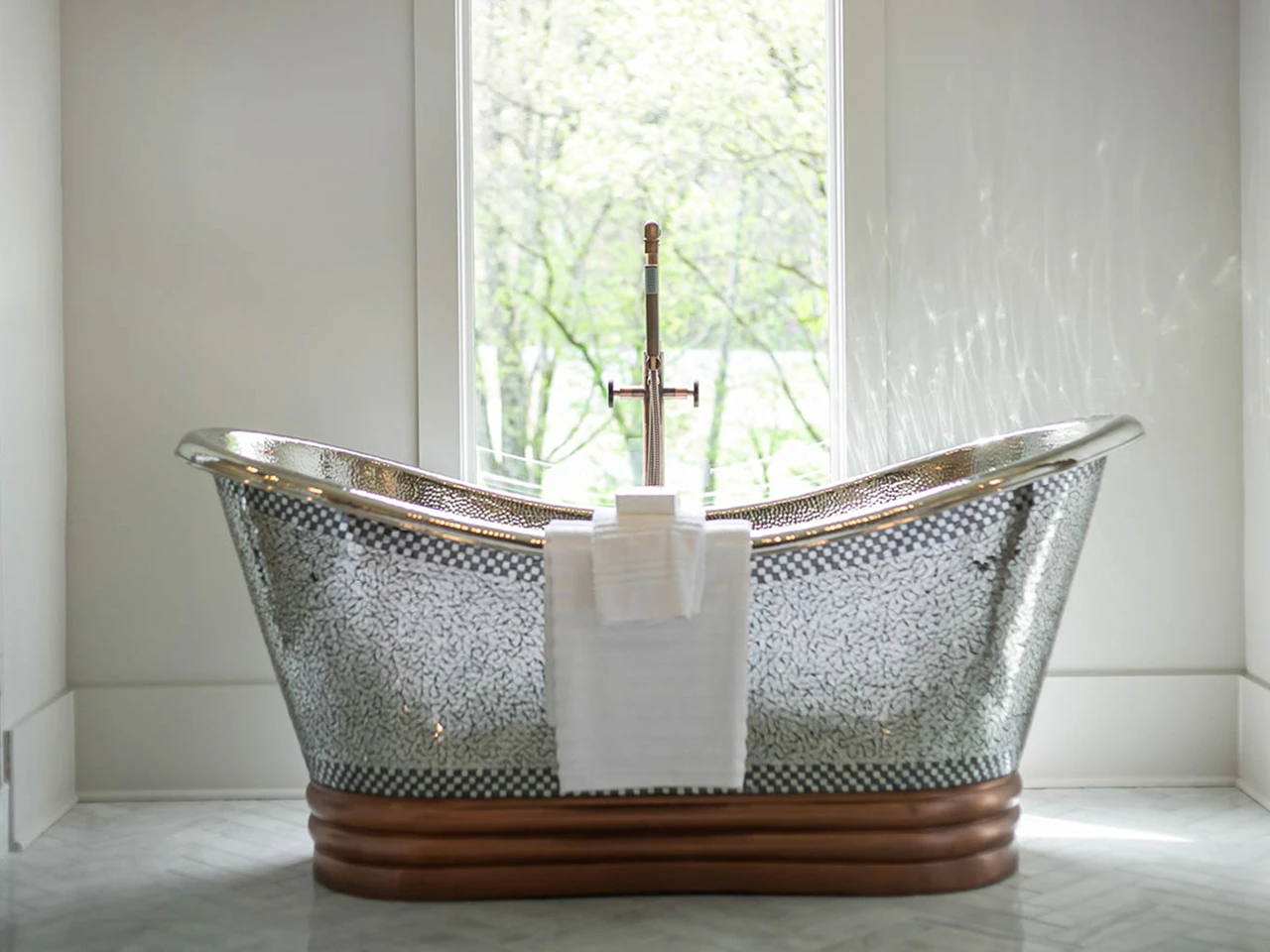 Freestanding metallic mosaic soaking tub positioned in front of a bright window