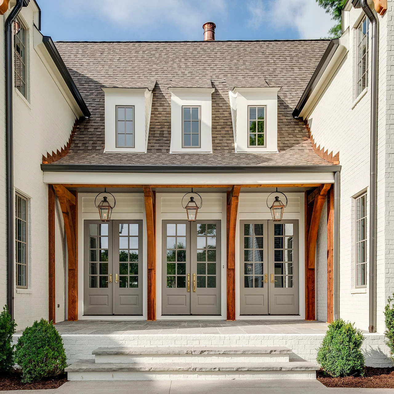 Home entry with covered porch, wood beams, French doors, and dormer windows above
