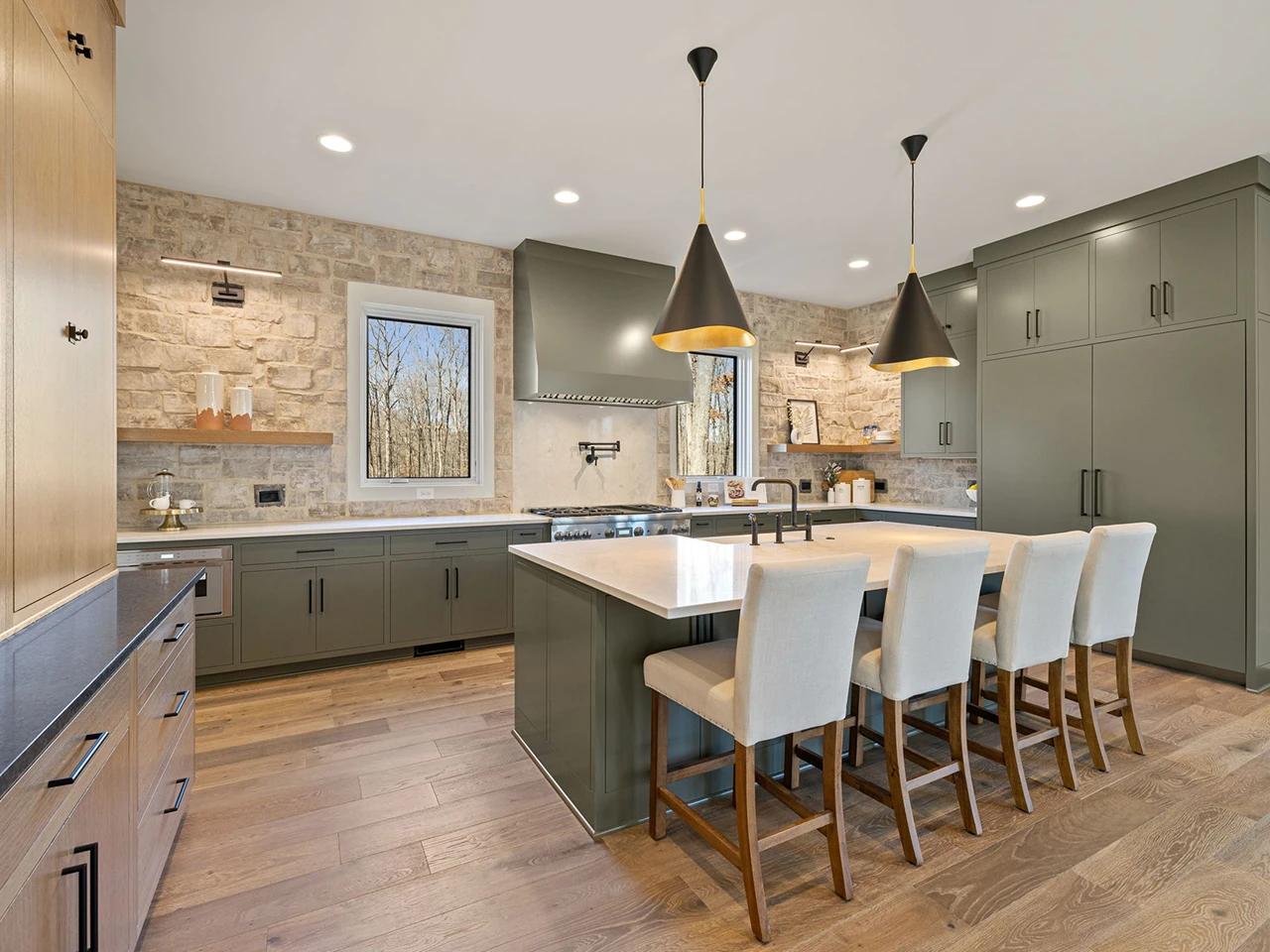 Kitchen with stone accent wall, olive green island, upholstered bar stools, and black dome pendant lights