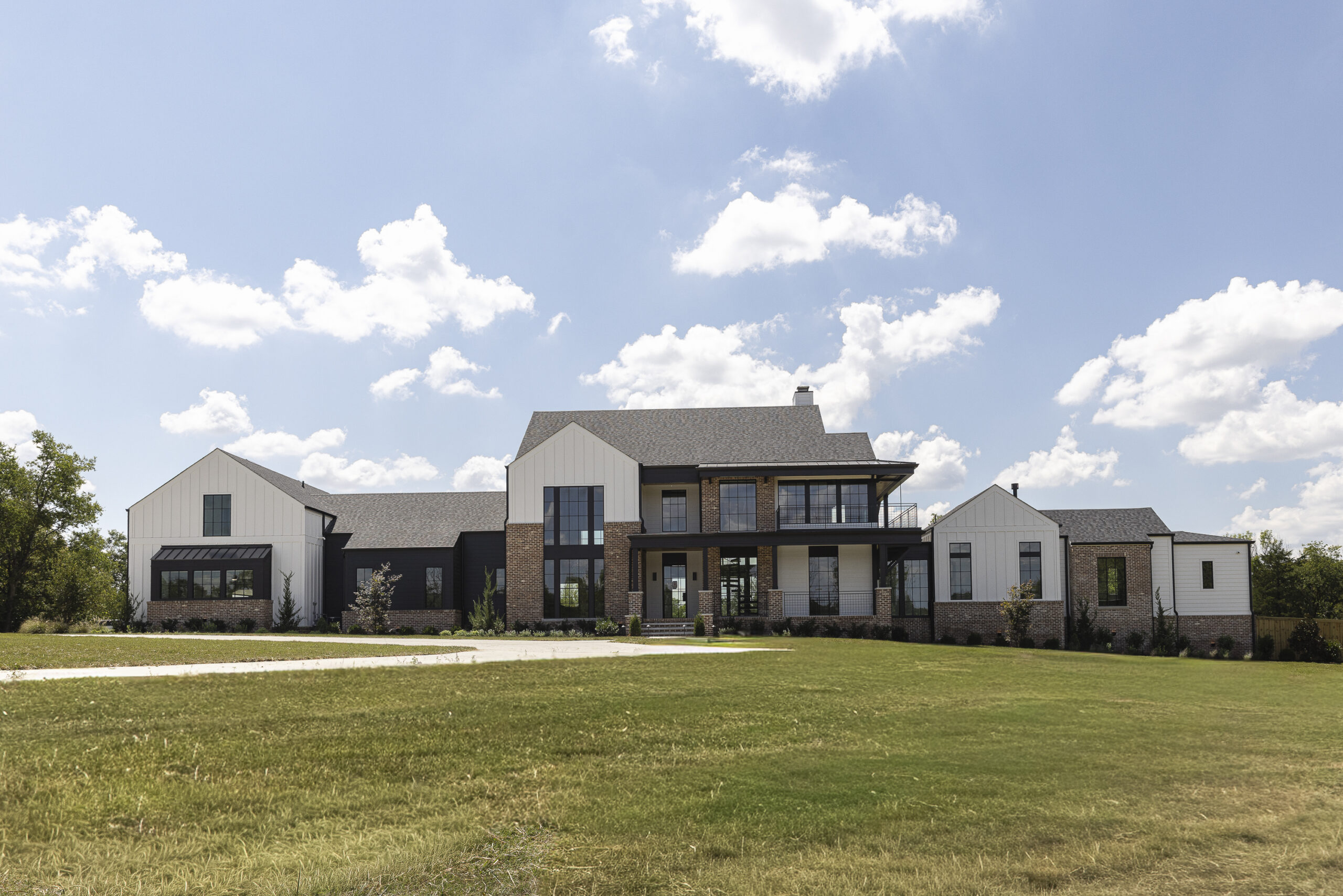 Two story modern farmhouse with white siding and brick with black metal porch railings and large windows
