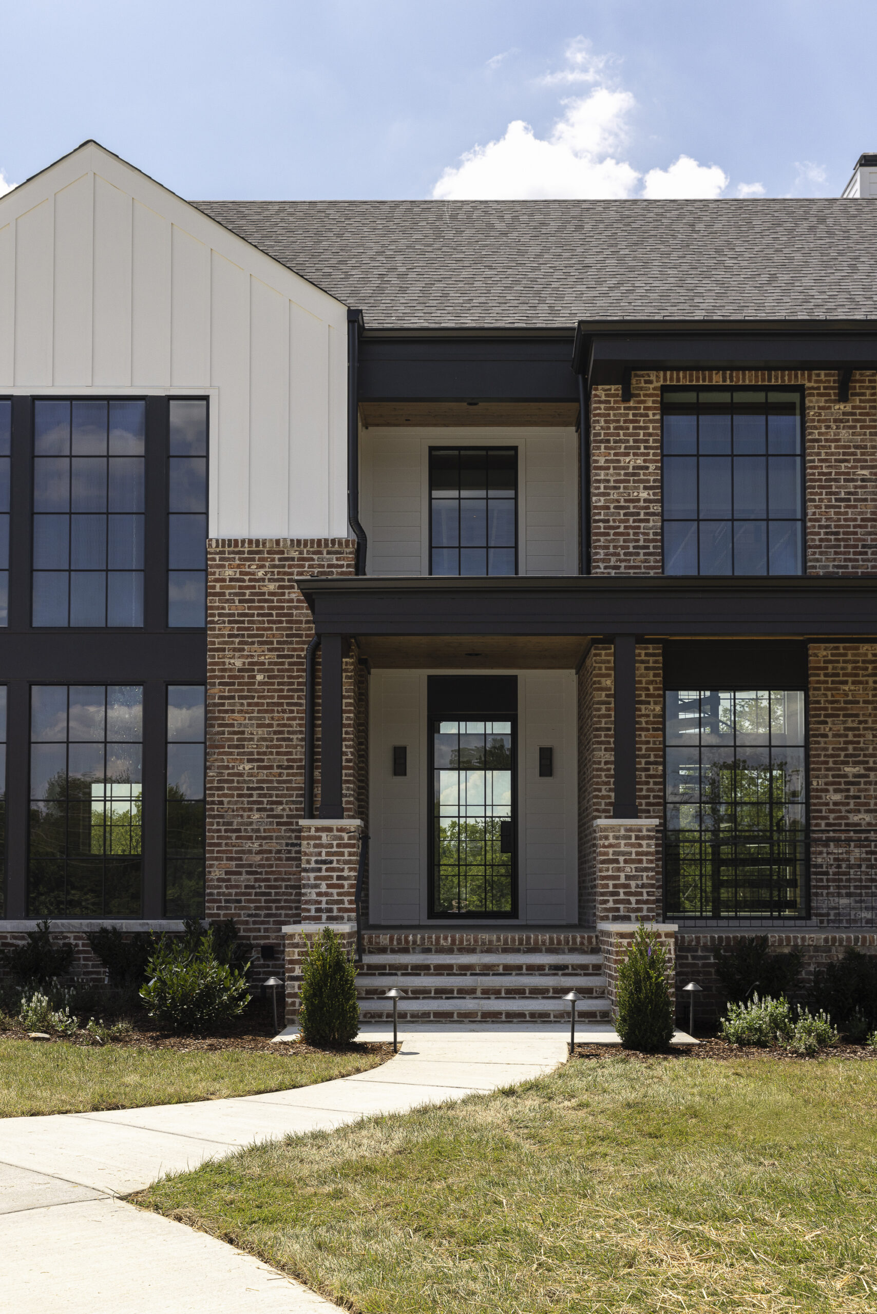 Two story modern farmhouse with white siding and brick with black metal porch railings and large windows
