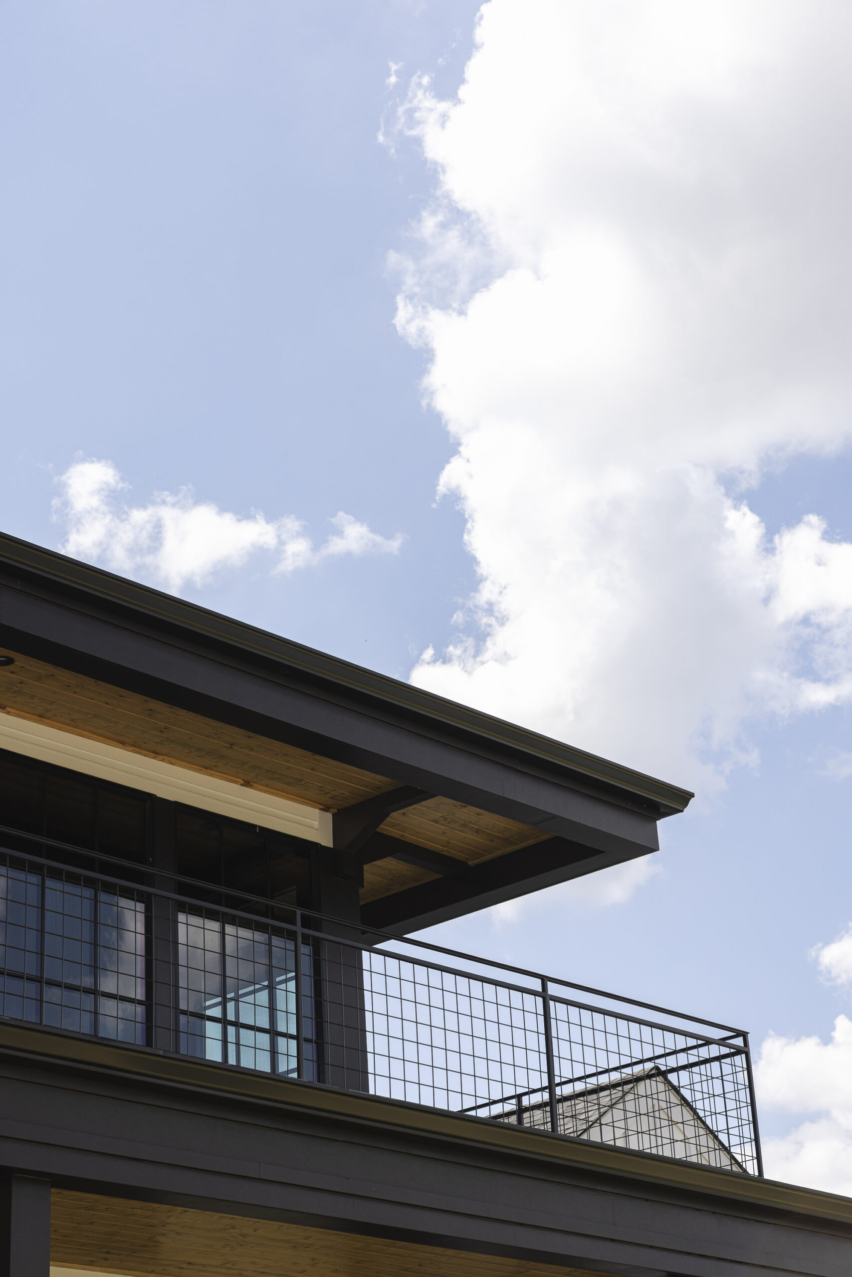 Upward picture of the roofline showing wooden overhangs and black metal porch railings and upper deck with large windows