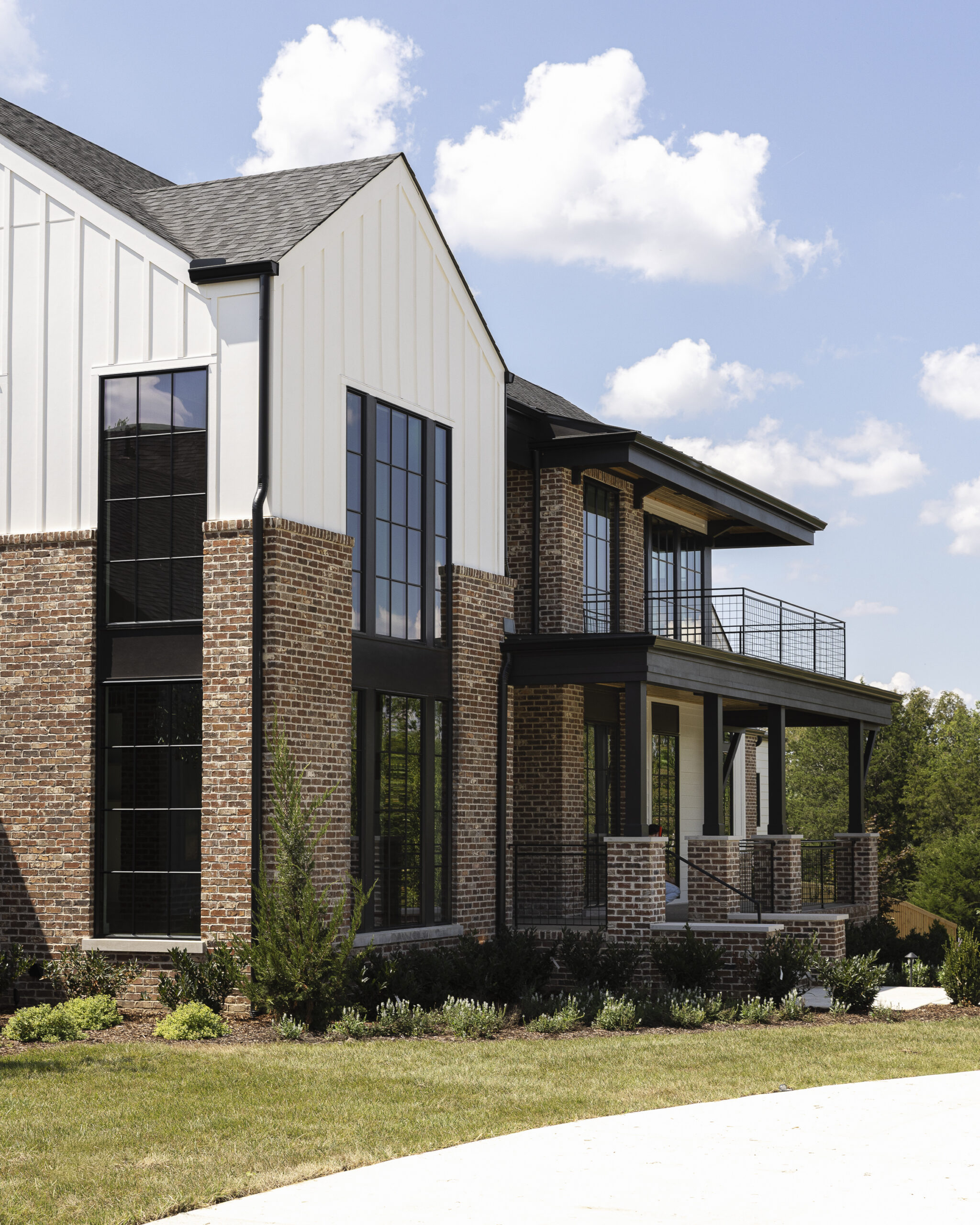 Two story modern farmhouse with white siding and brick with black metal porch railings and large windows