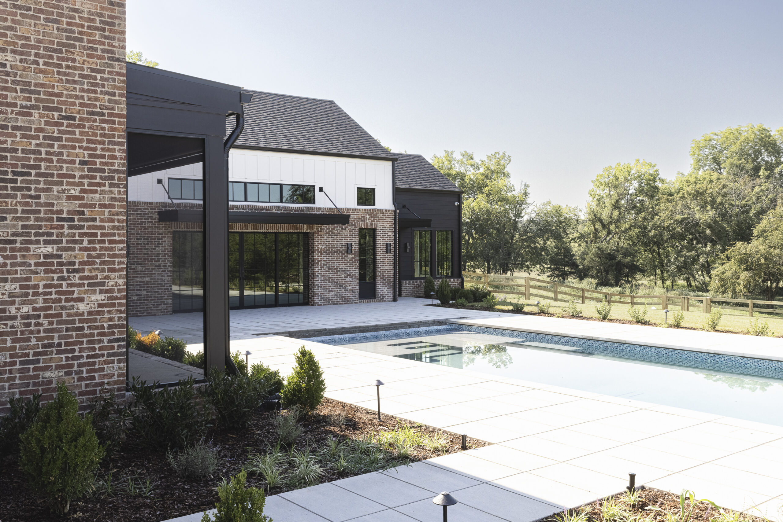 Two story modern farmhouse with white siding and brick with black metal porch railings and large windows and a large rectangular pool