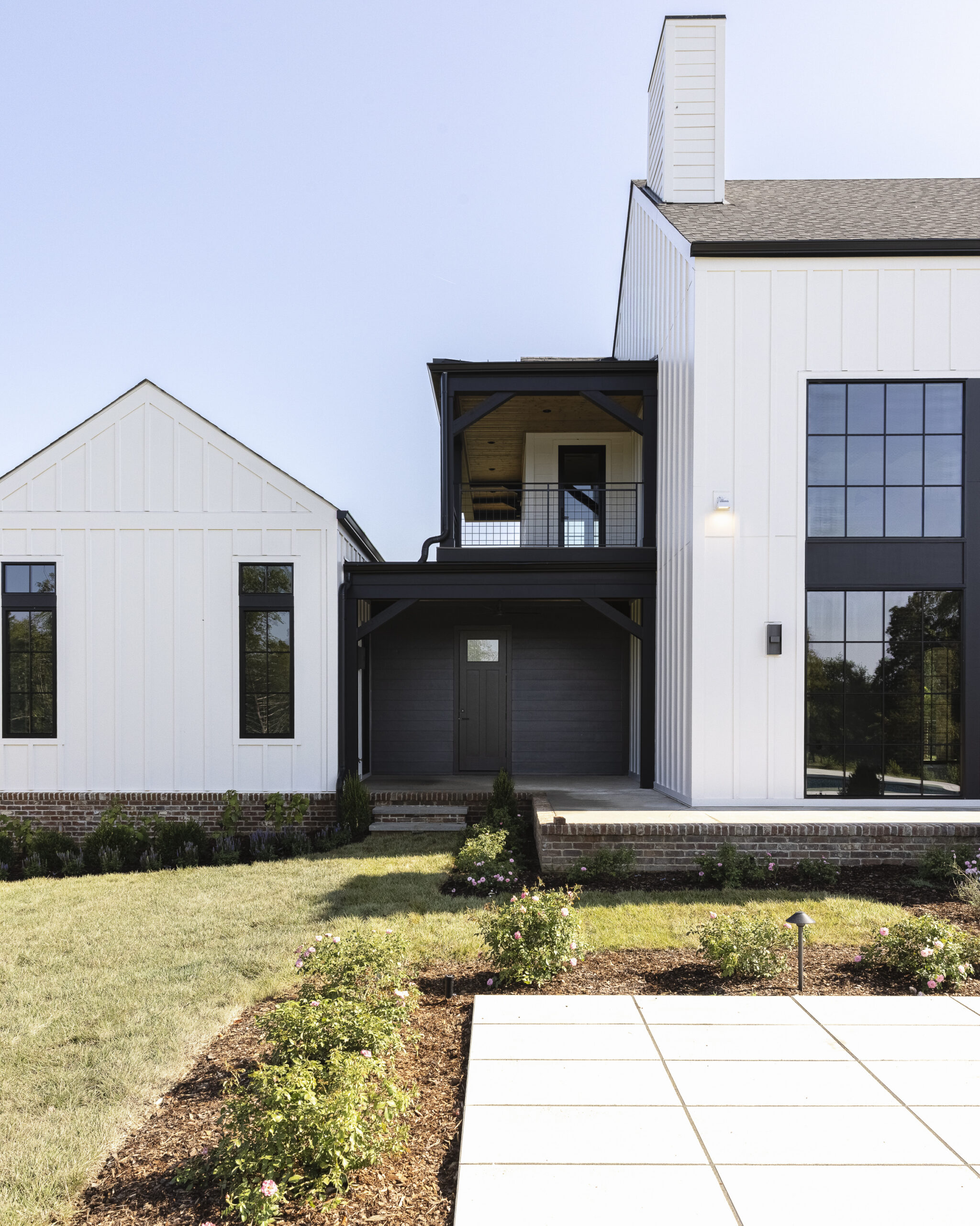 Two story modern farmhouse with white siding and brick with black metal porch railings and large windows