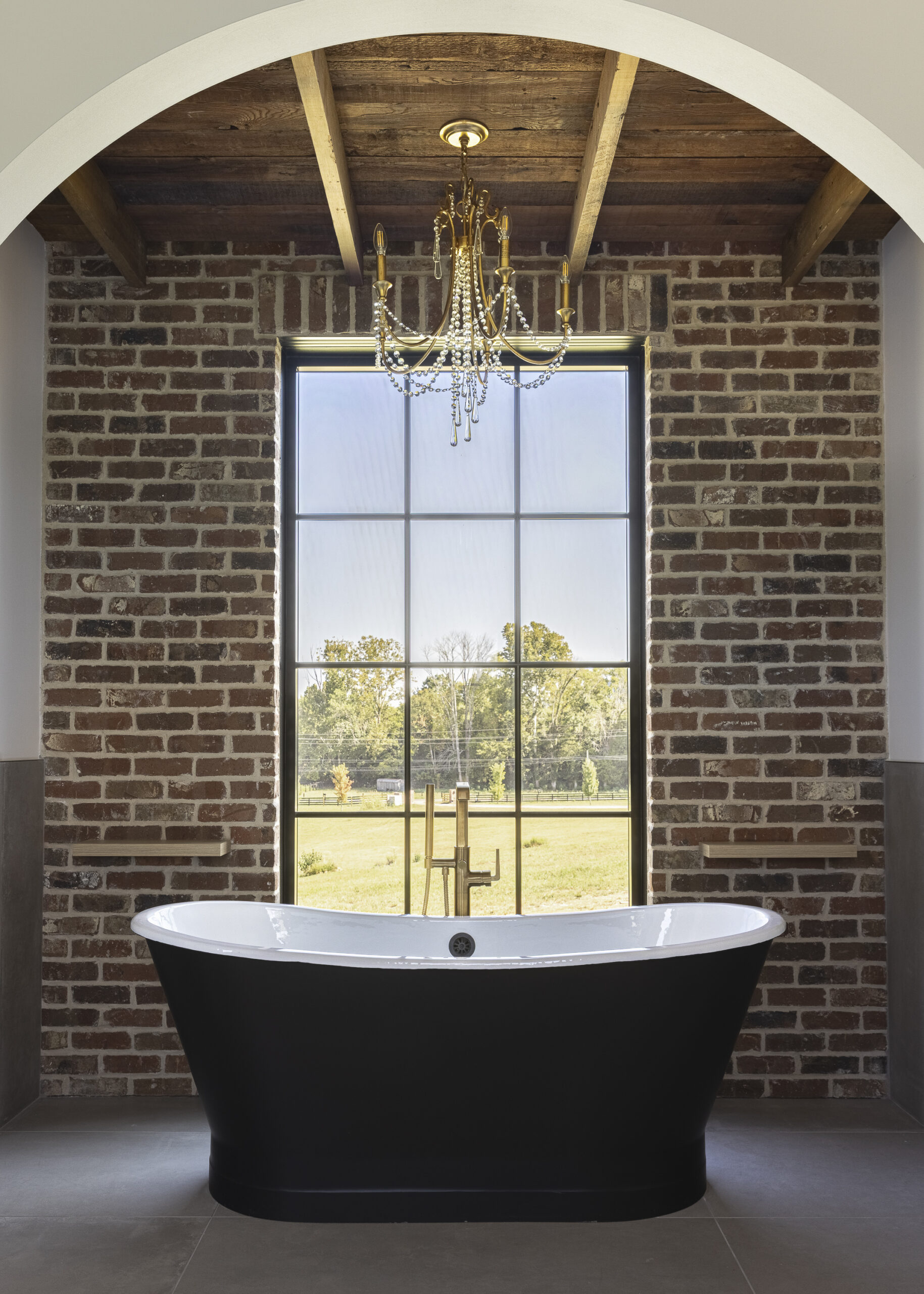 Dark brick wall with a large window with grids and a black metal tub framed by an arch with an exposed wood ceiling