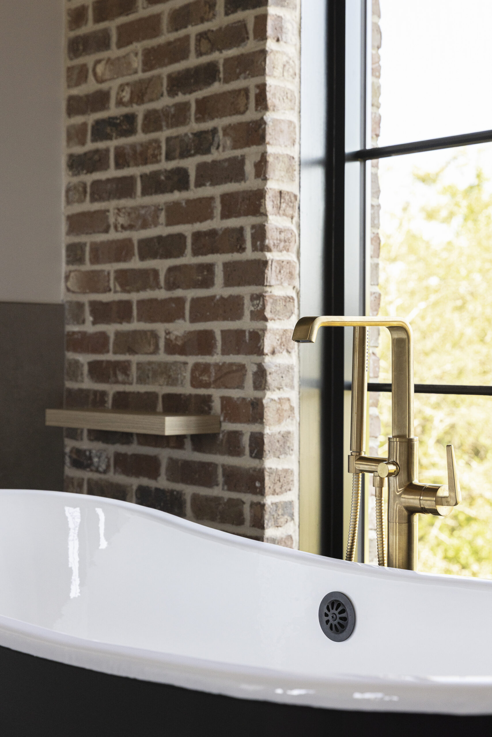 Dark brick wall with a large window with grids and a black metal tub