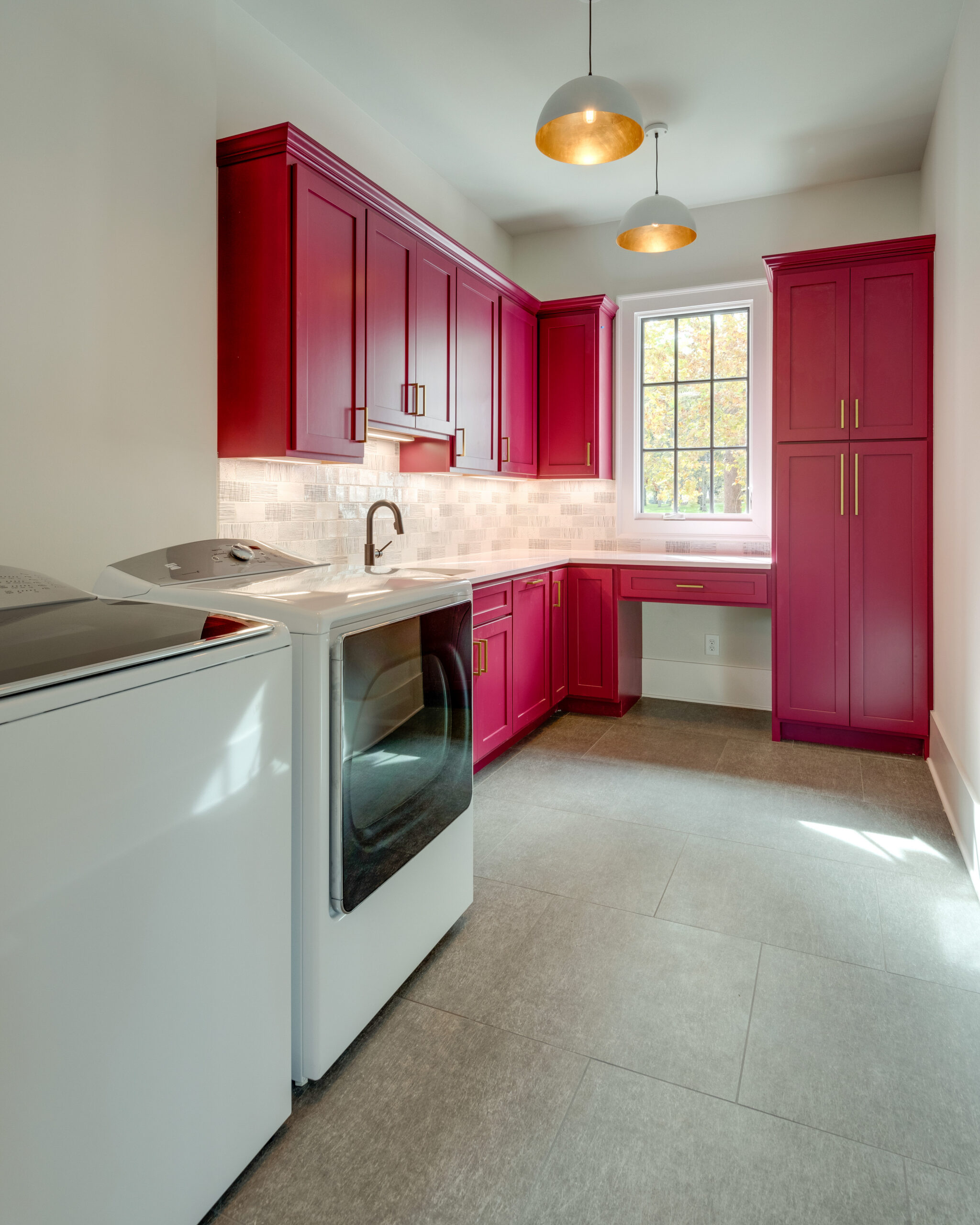 Large walkin laundry room with bright fuchsia cabinets and two chandliers with a single window and white walls