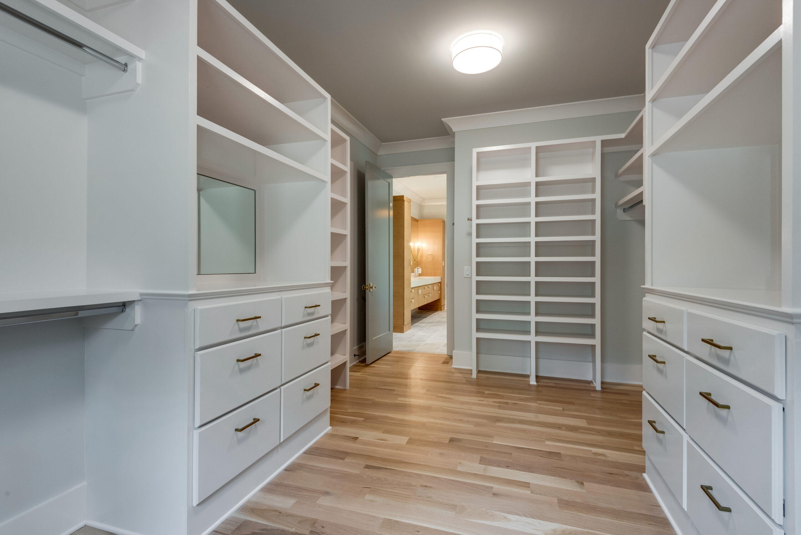 Large white walk-in closet with open shelving, and drawers for storage under a window with a light