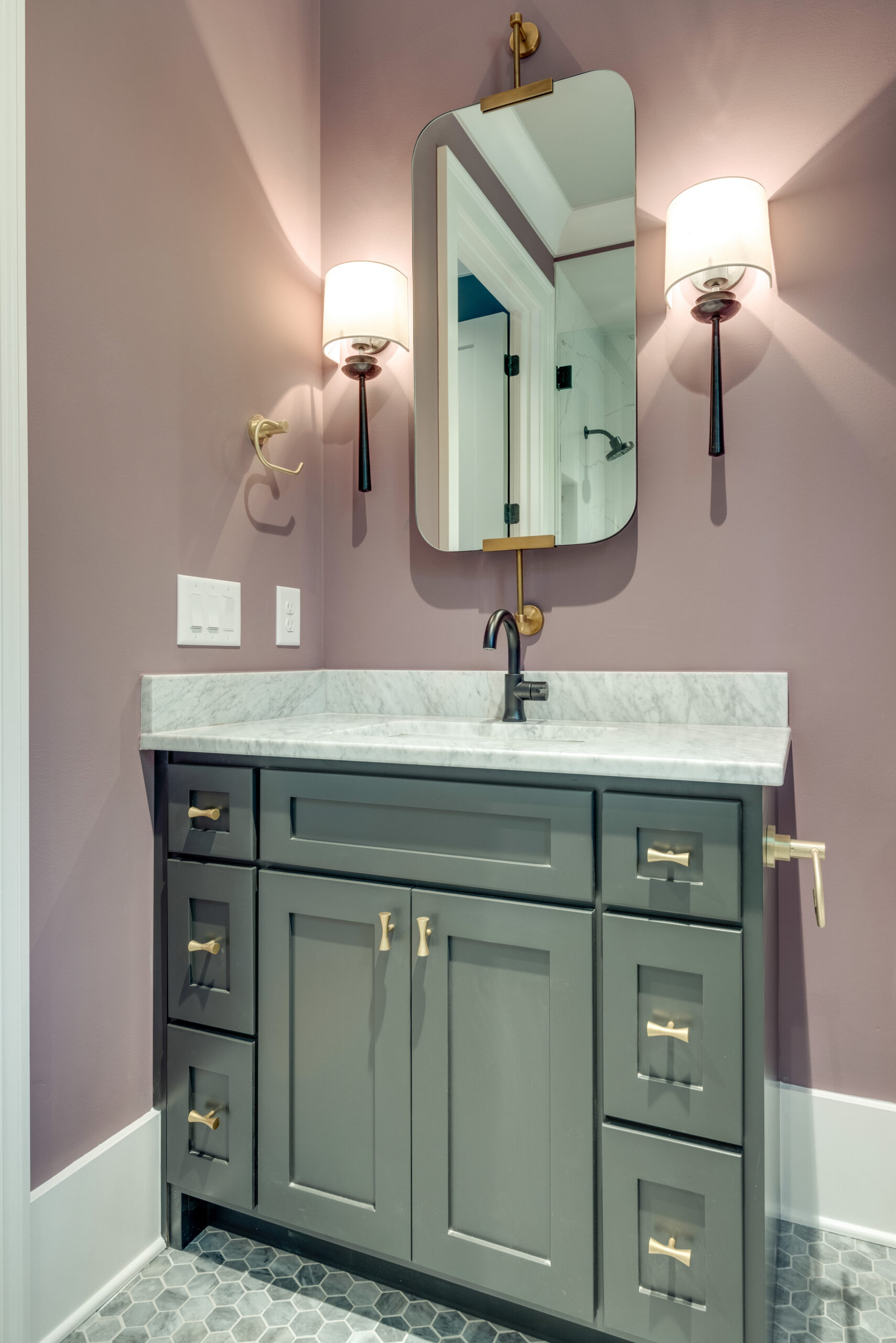 Powder bathroom with mauve walls and deep green painted vanity with white countertops, a mirror, and sconces